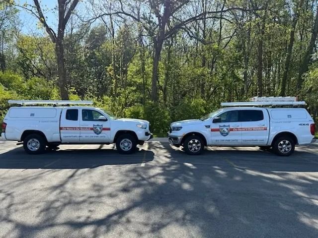 Two white service vans parked side by side on a tree-lined street in daylight