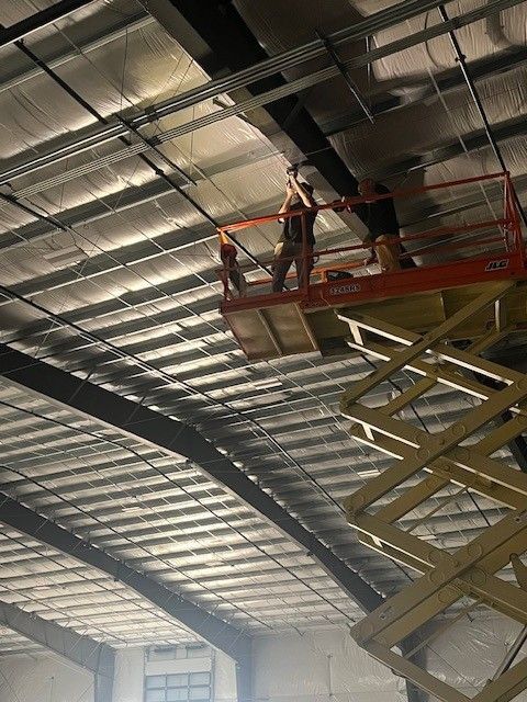 Workers on a red scissor lift inspecting the ceiling of a large warehouse.