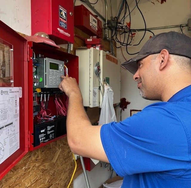 Technician inspecting electrical control panel with wiring in a red utility box