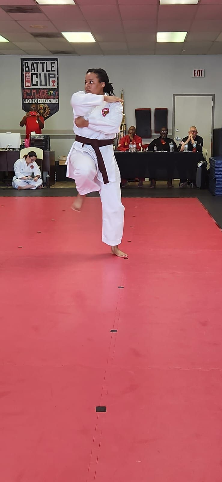 Martial artist in white uniform performing a high kick on a red mat in an indoor gym