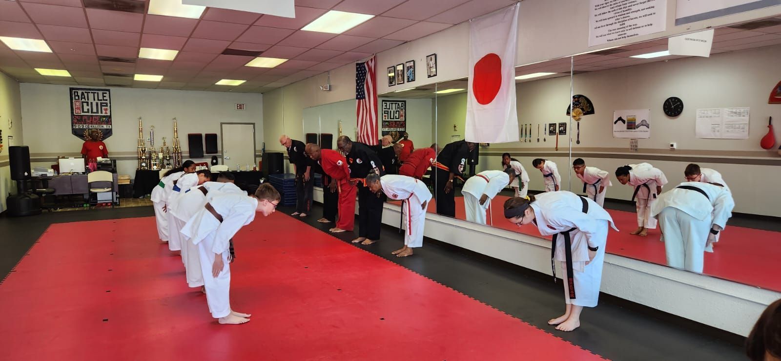 Martial arts class in white uniforms bowing on a red mat inside a dojo