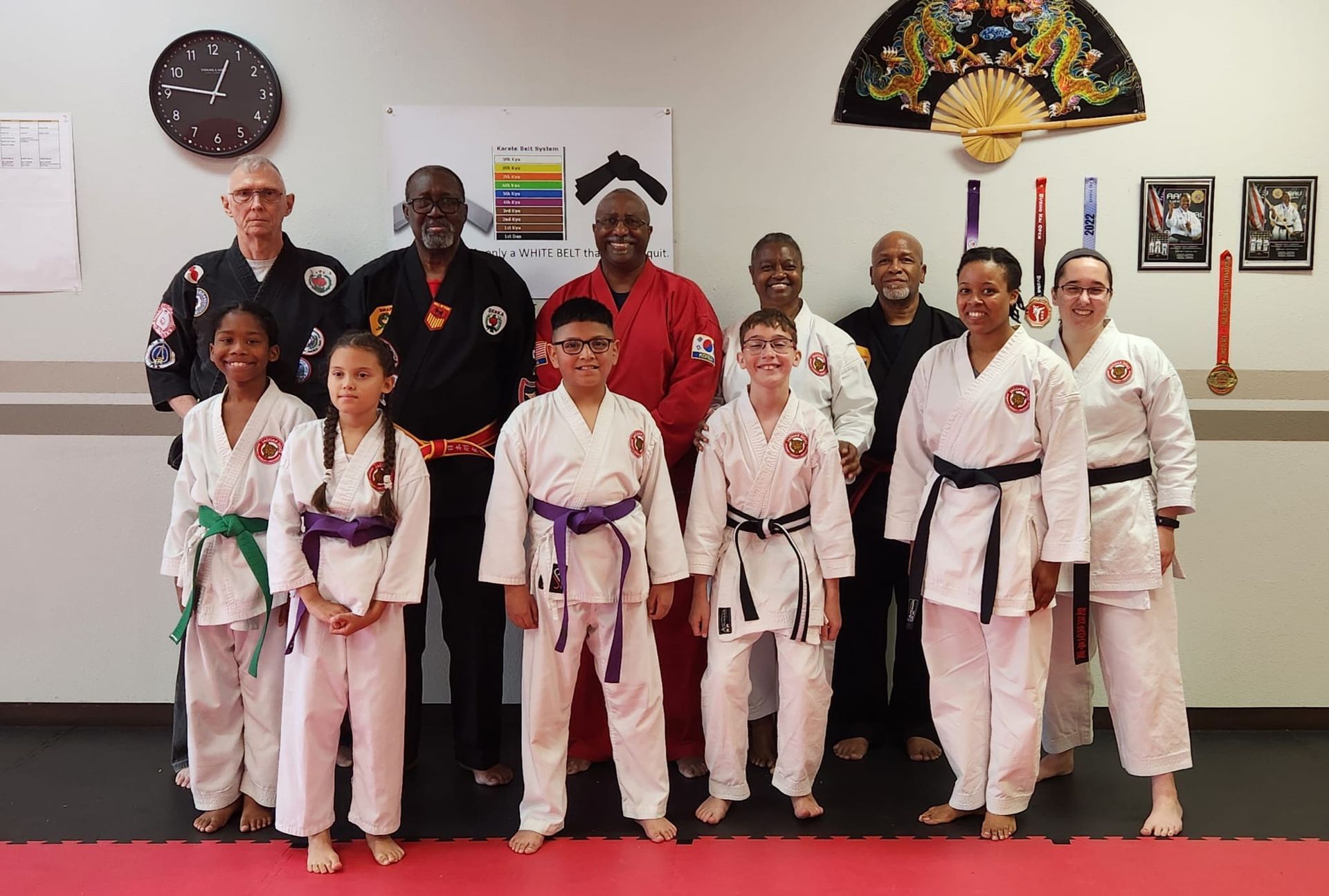 Martial arts class posing in white gis and belts inside a dojo with wall art and clocks