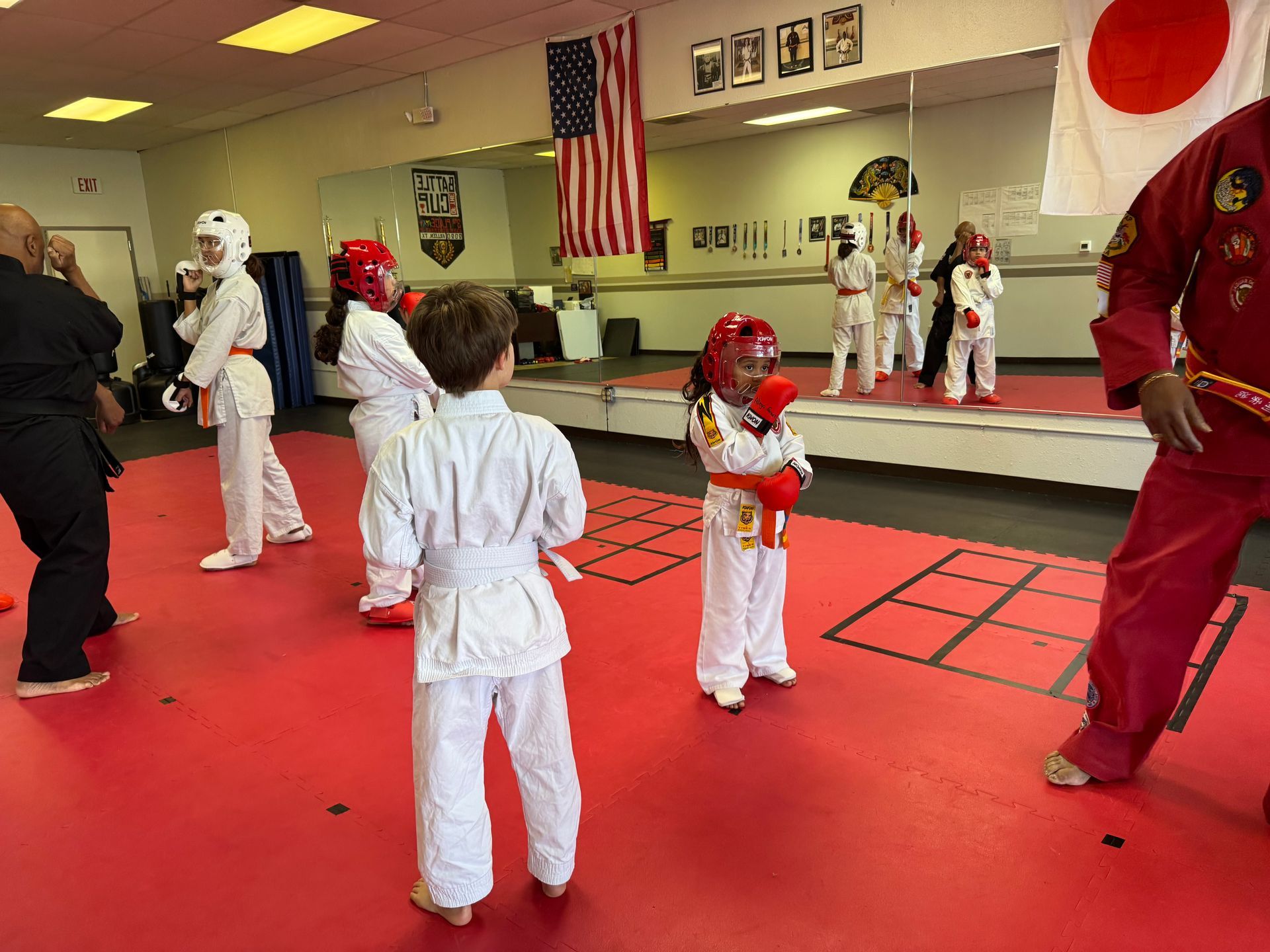 Martial arts class practicing in a mirrored studio with red mats and uniforms