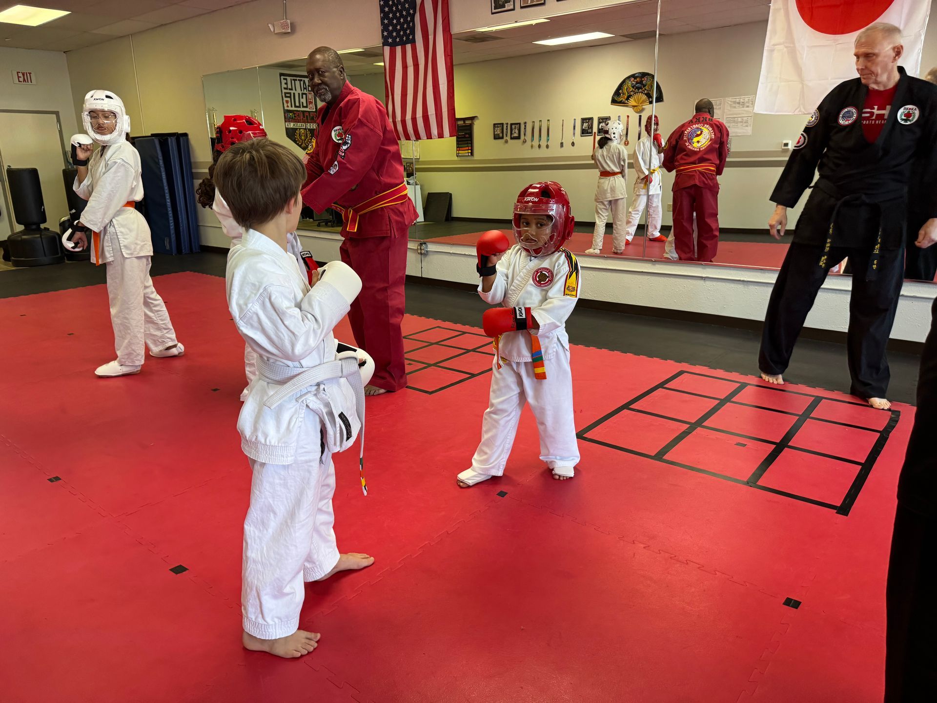 Children practicing martial arts in a dojo, with instructors and a red training floor.