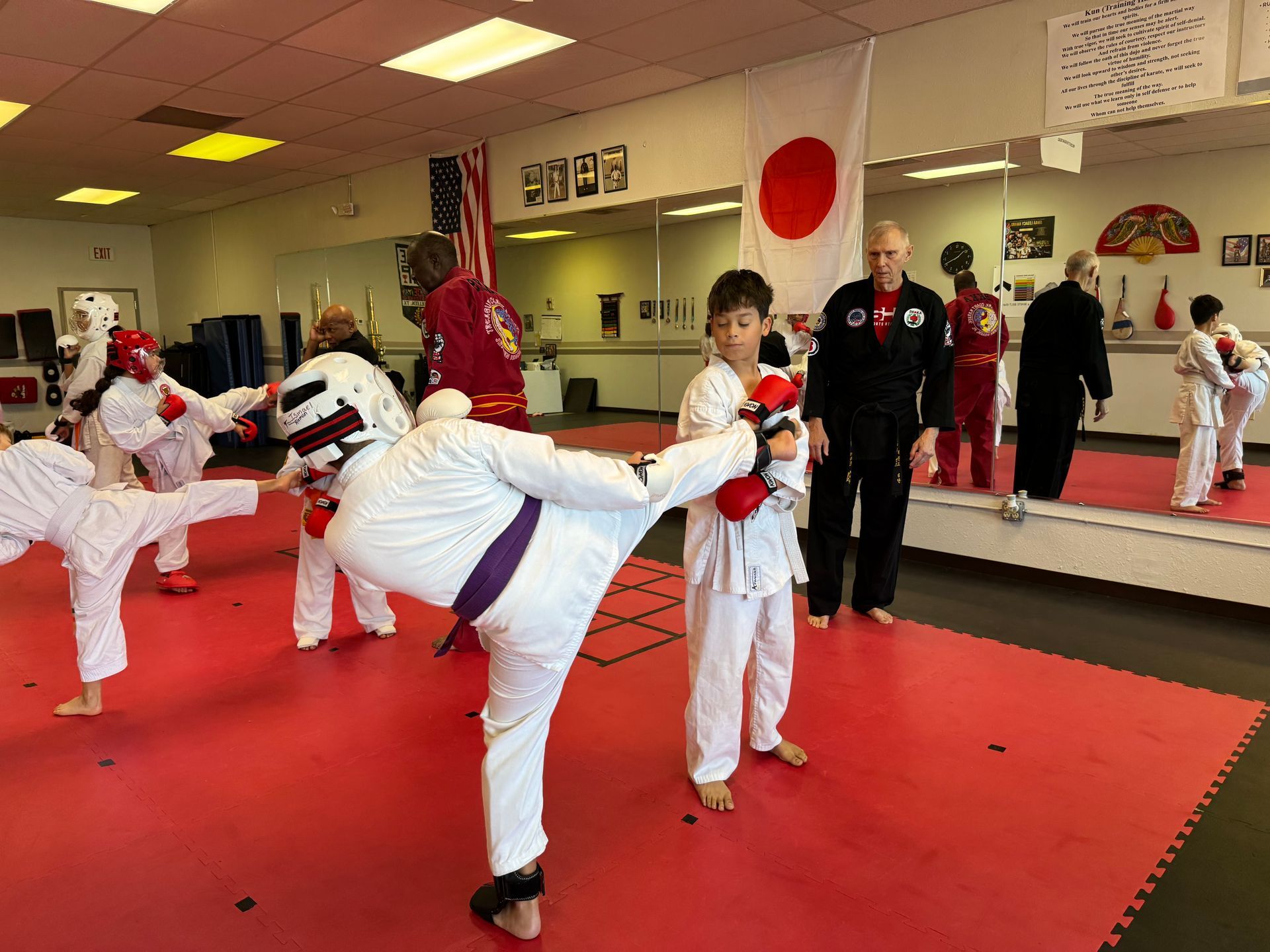 Martial arts class with children in white uniforms practicing kicks on red mats in a mirrored studio