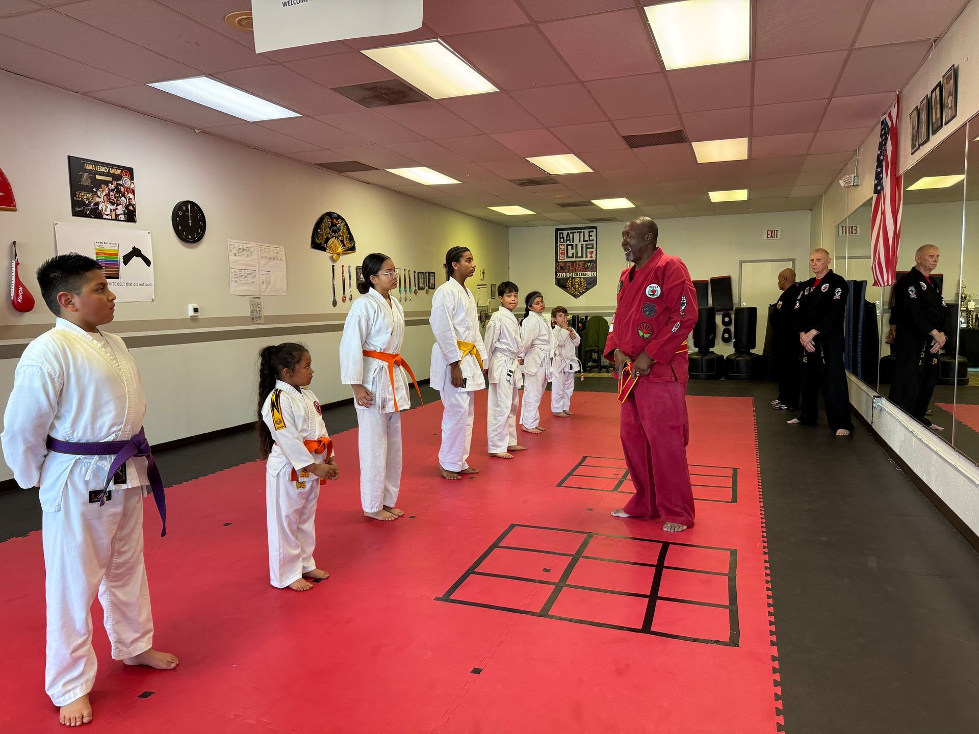Martial arts class lined up on red mats as an instructor demonstrates a stance in a studio
