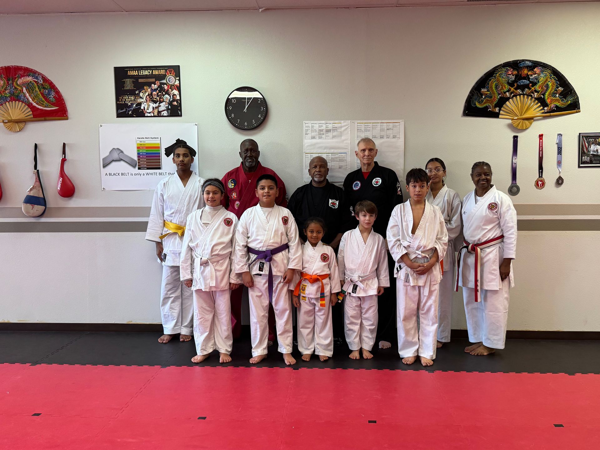 Martial arts class posing in white uniforms on a red mat inside a studio