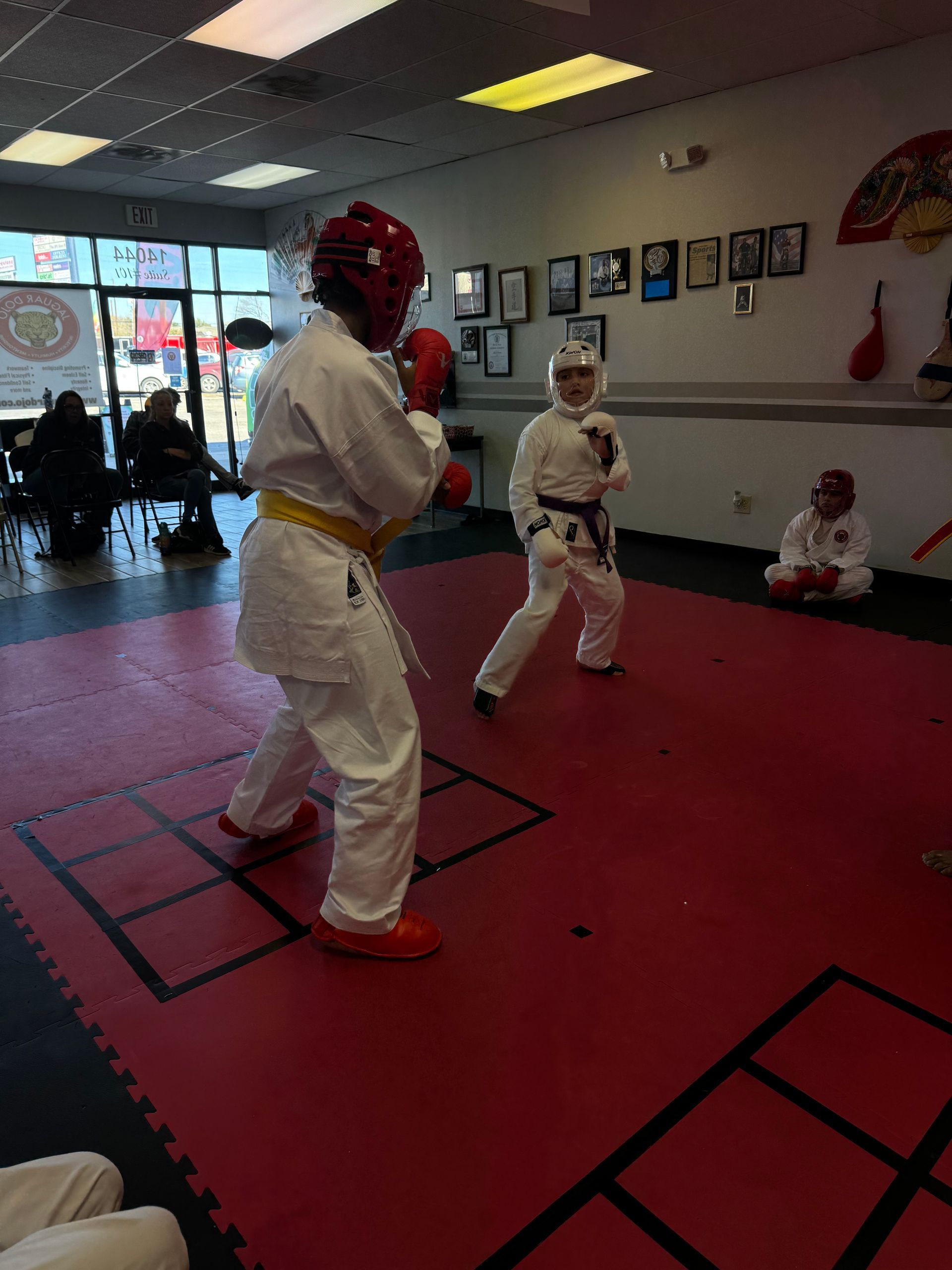 Two martial arts students sparring in white uniforms on a red mat in a dojo