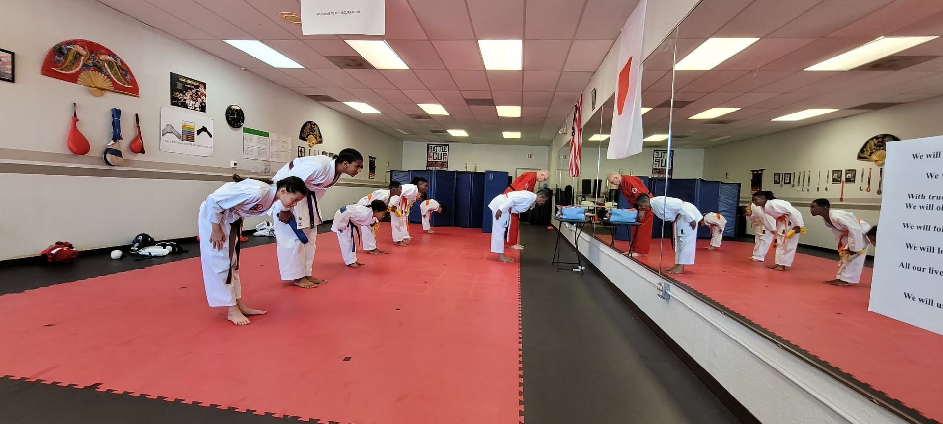 Martial arts class bowing on red mats in a mirrored studio, with instructors and students lined up.