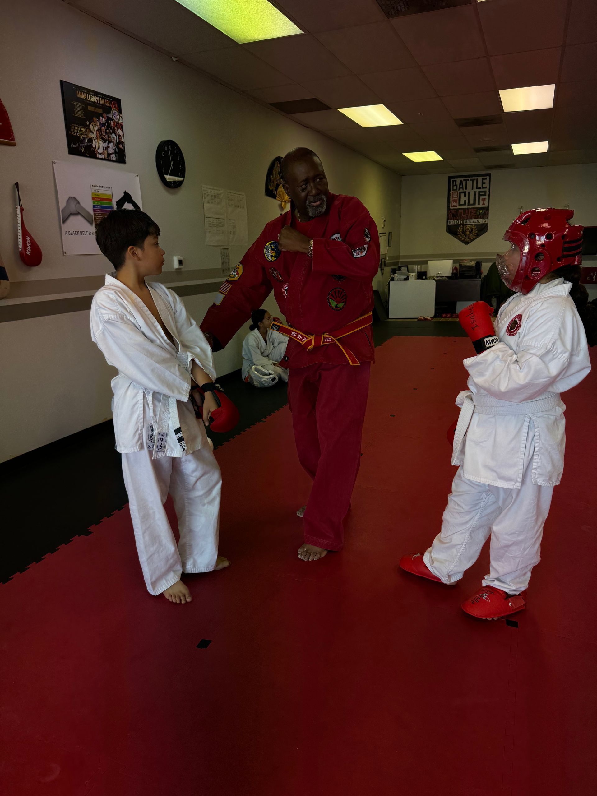 Martial arts instructor in red guiding two students in white uniforms in a dojo