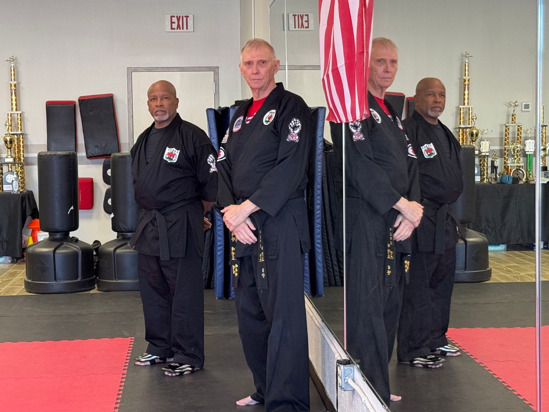 Martial arts class posing in a studio with mirrored walls, trophies, and red training mats