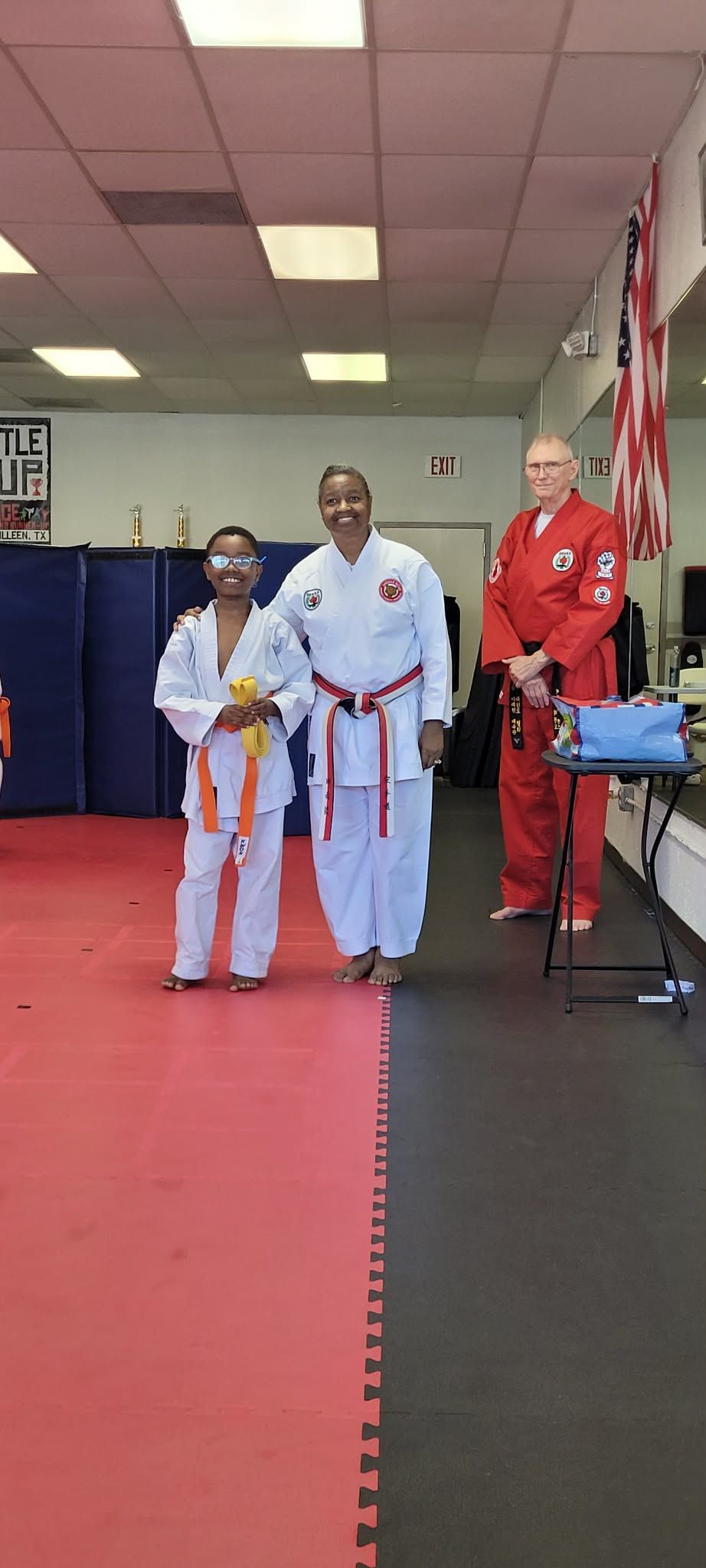 Martial arts awards ceremony with three people in white and red uniforms on a padded studio floor