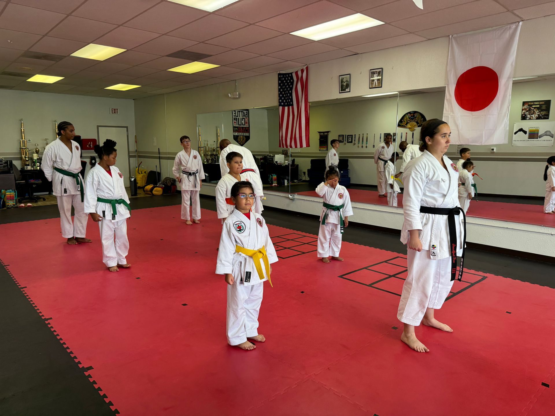 Martial arts class practicing on red mats in a dojo with Japanese flags on the wall