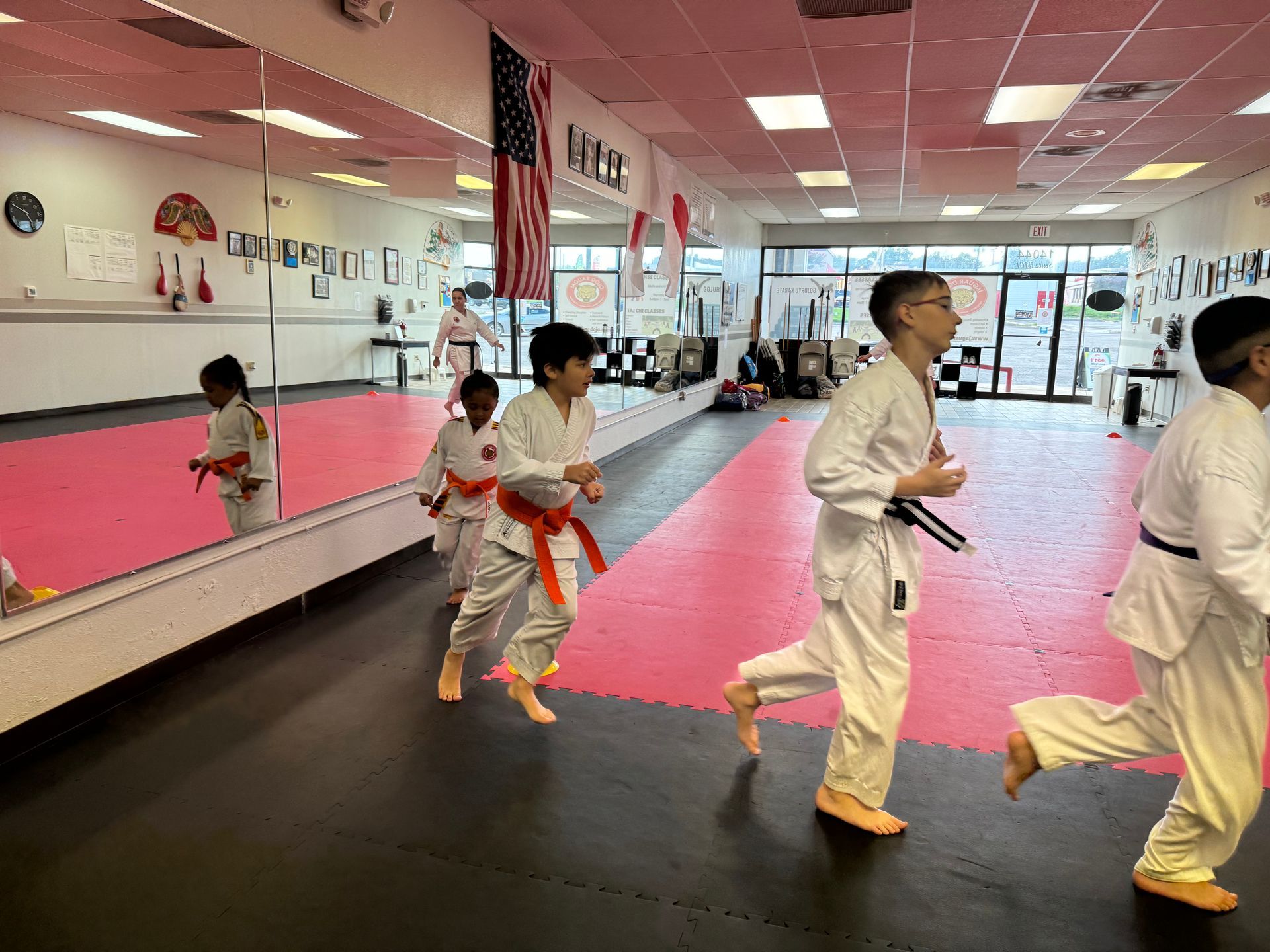 Kids practicing martial arts in a mirrored studio with pink mats and flags hanging overhead