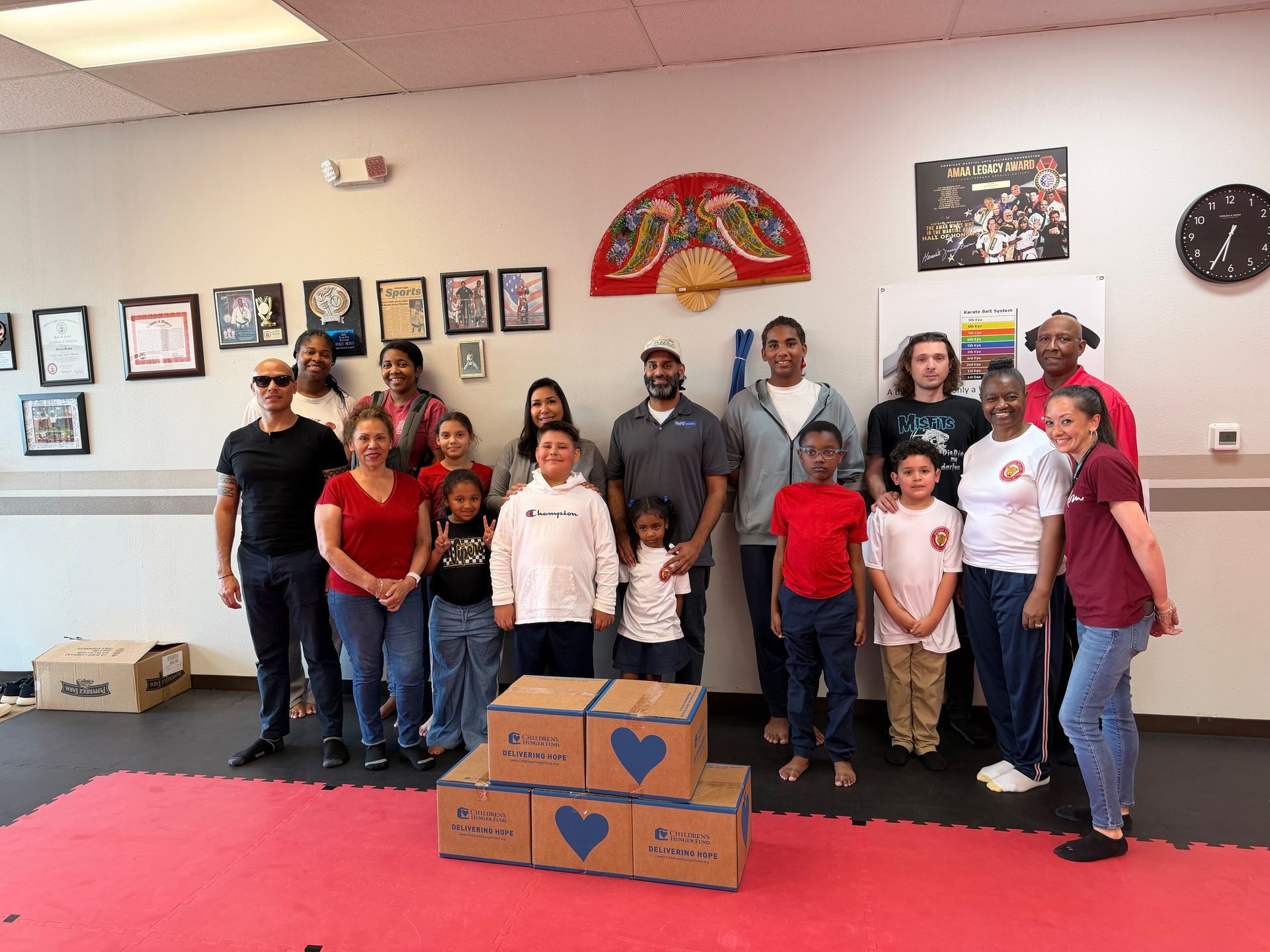 Group of volunteers posing indoors with boxes of donated items and framed photos on the wall.