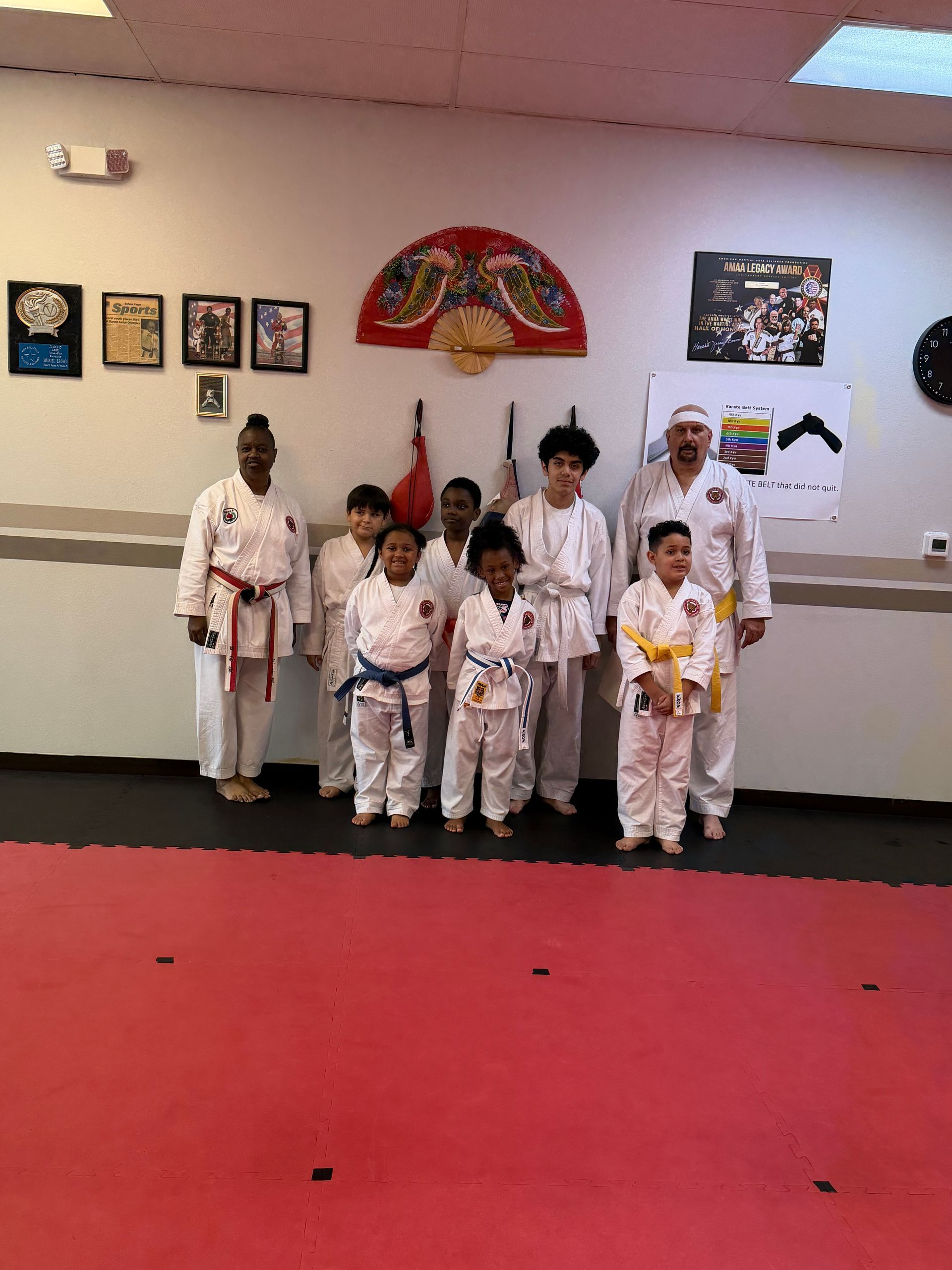 Martial arts class posing in white uniforms on a red mat in a dojo with wall decorations