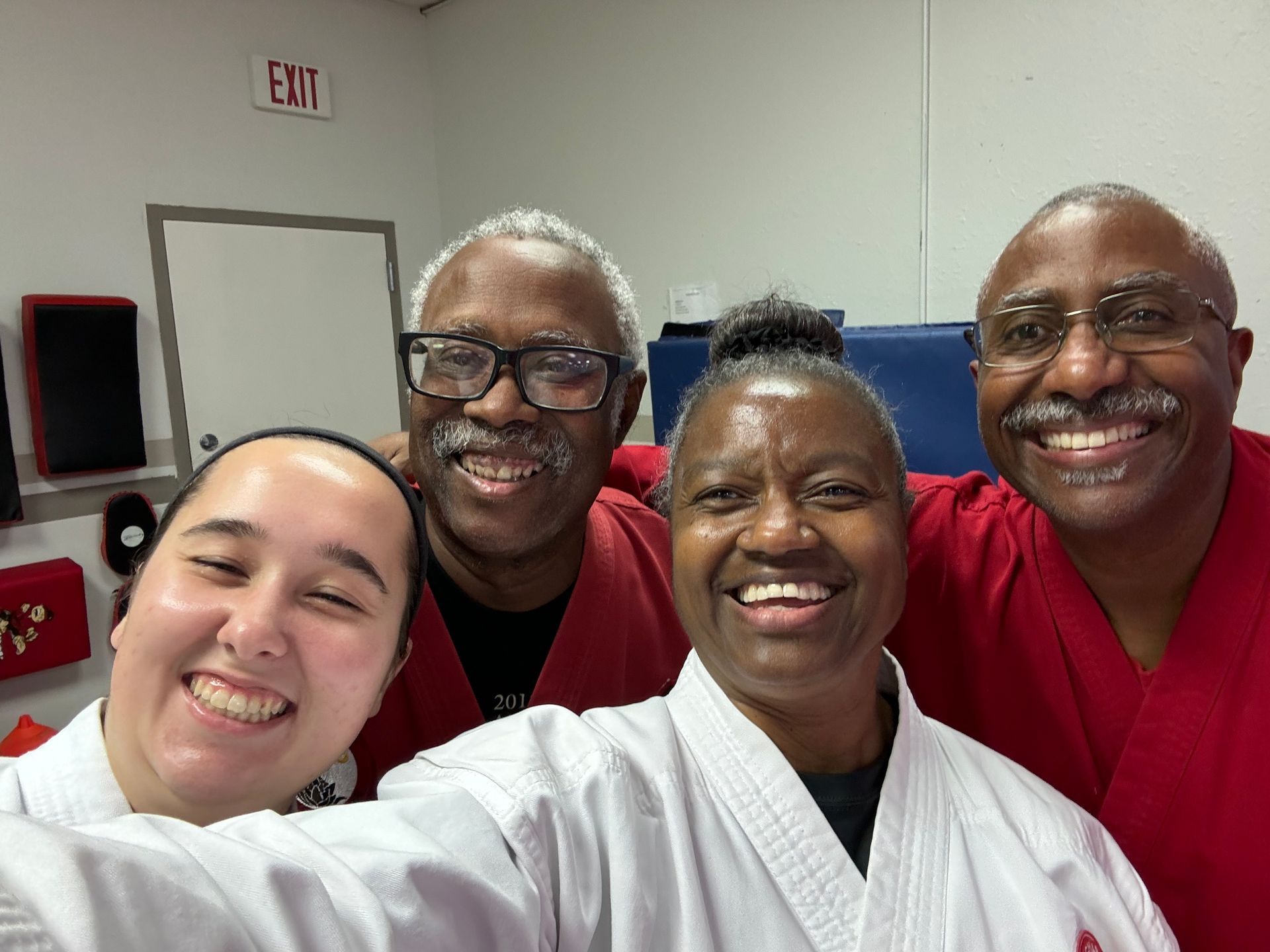 Four smiling staff members in red and white uniforms pose together indoors, taking a selfie.
