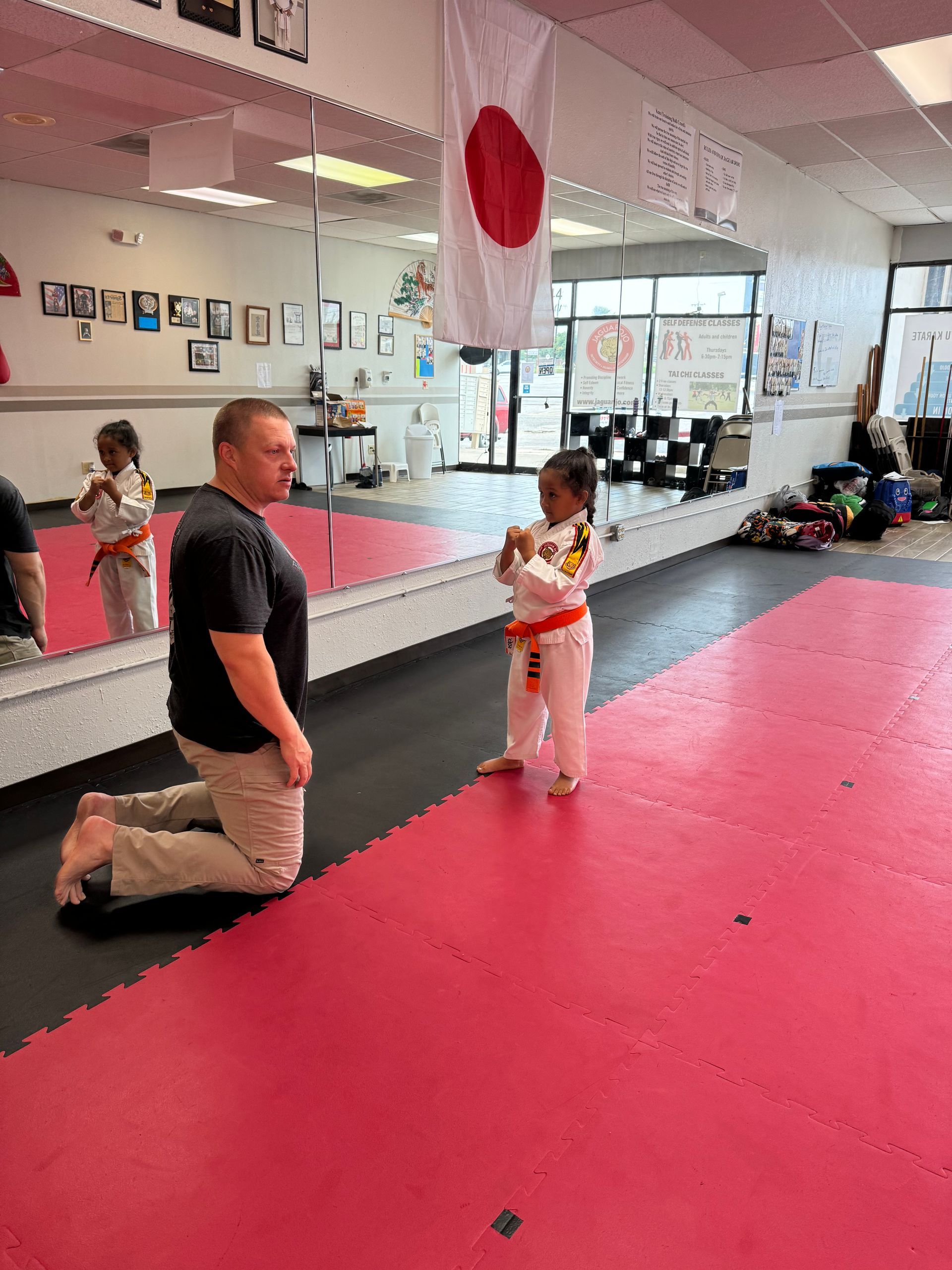 Martial arts studio with a kneeling instructor and a child holding a Japanese flag near a mirror wall