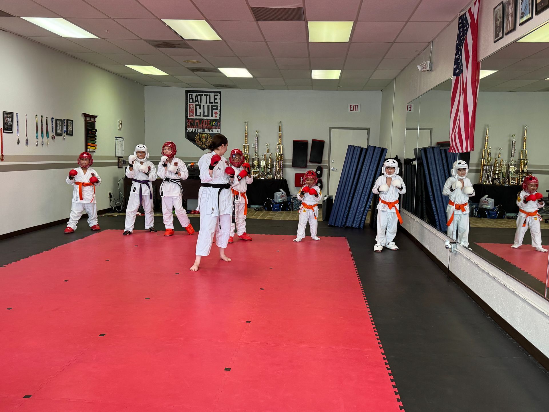 Children practicing martial arts in a dojo with red mats and mirrors