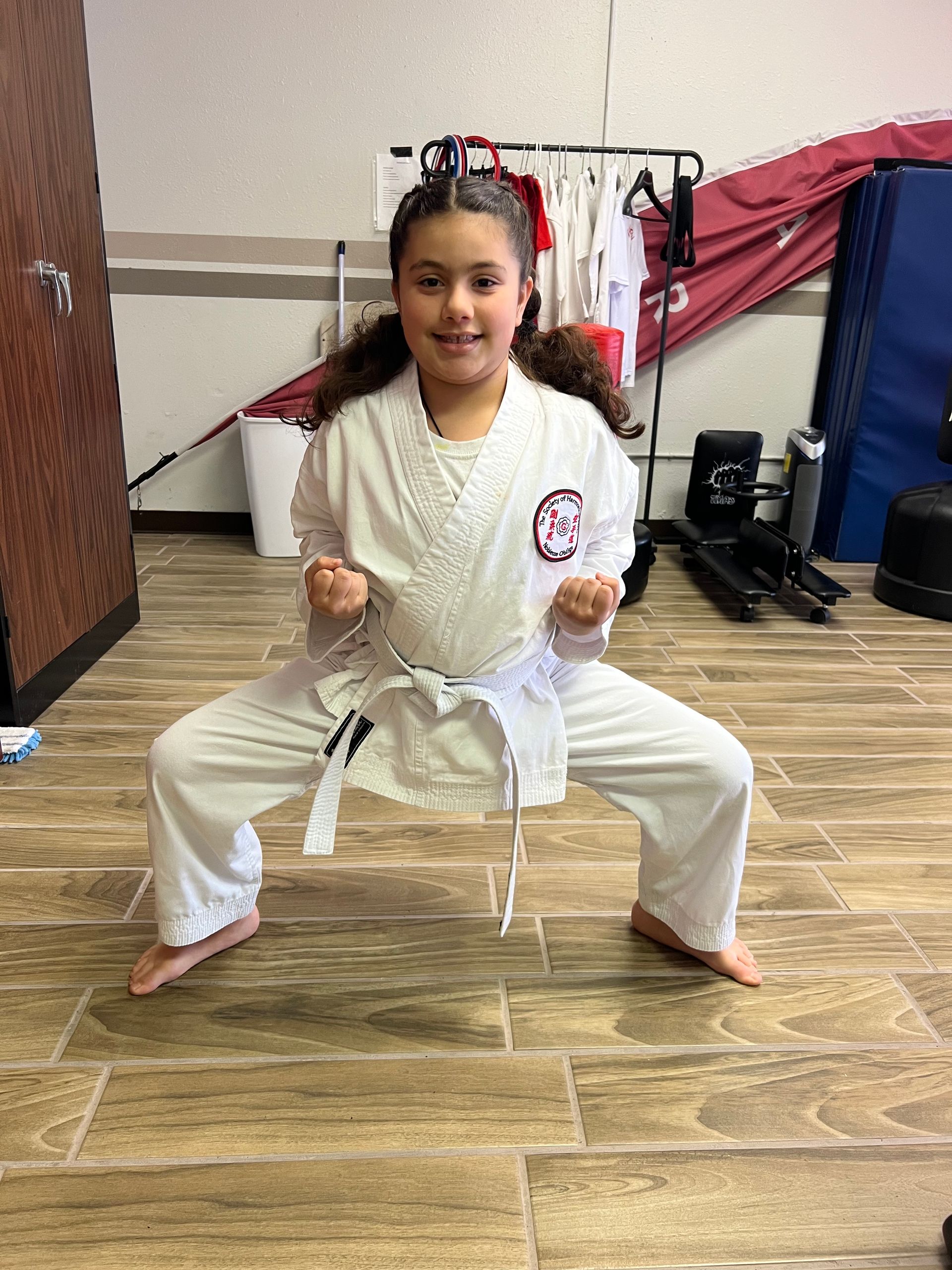 Person in a white martial arts uniform and red gloves in a low stance on a dojo floor.