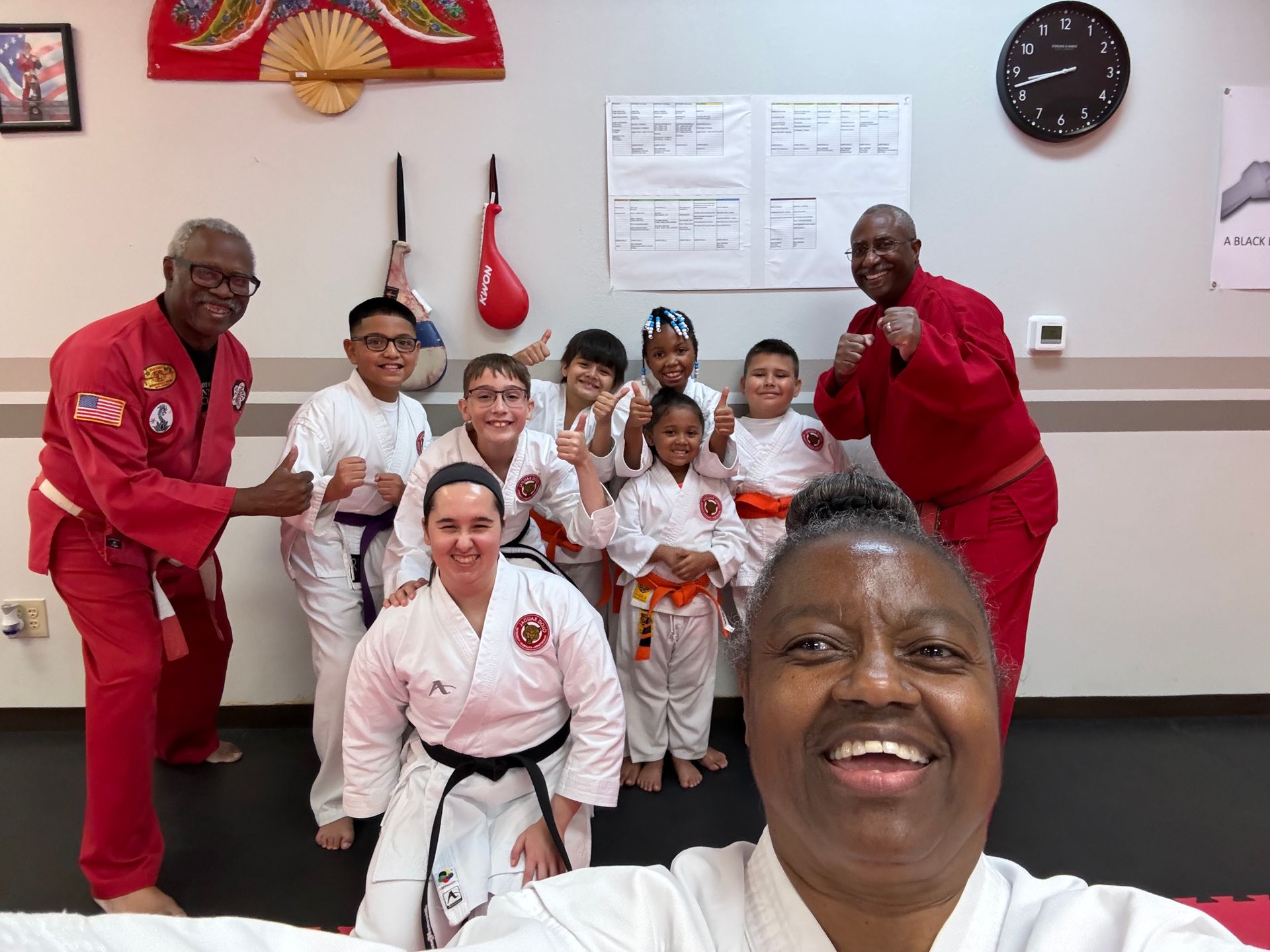 Martial arts class group posing in a dojo, smiling and wearing white uniforms and red jackets.