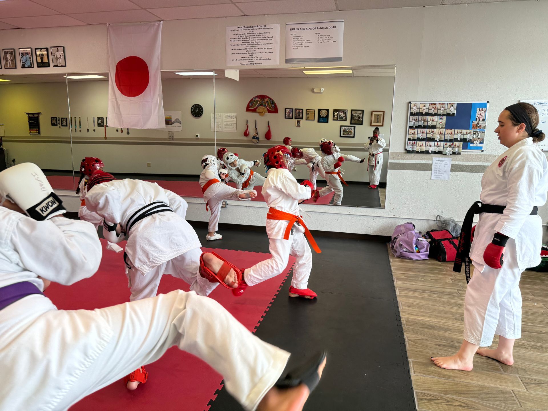 Karate class practicing kicks and stances in a mirrored dojo with red mats and Japanese flag