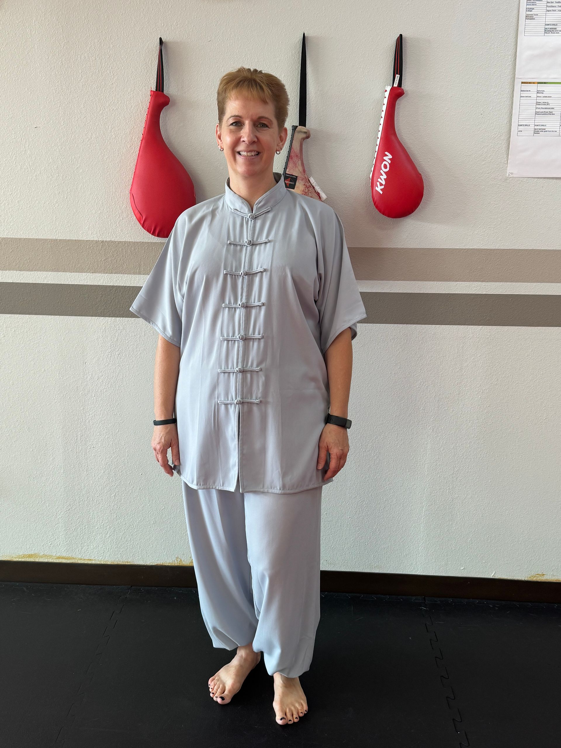 Person in light gray traditional attire standing barefoot against a wall with red hanging decor.