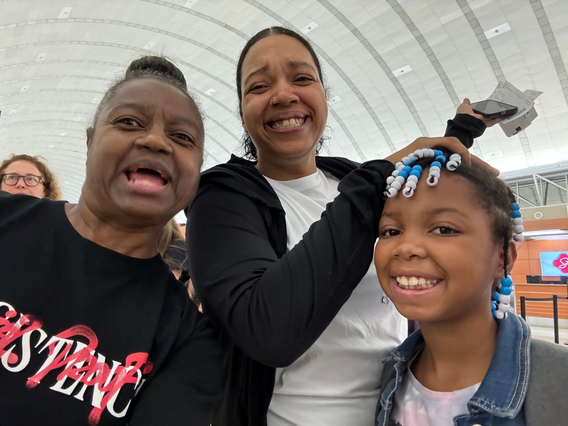 Three people smiling indoors, posing for a selfie under a curved glass ceiling.