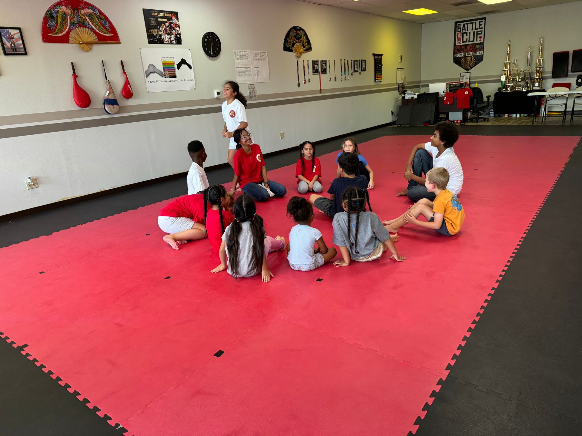 Children sitting in a circle on red mats in a martial arts studio