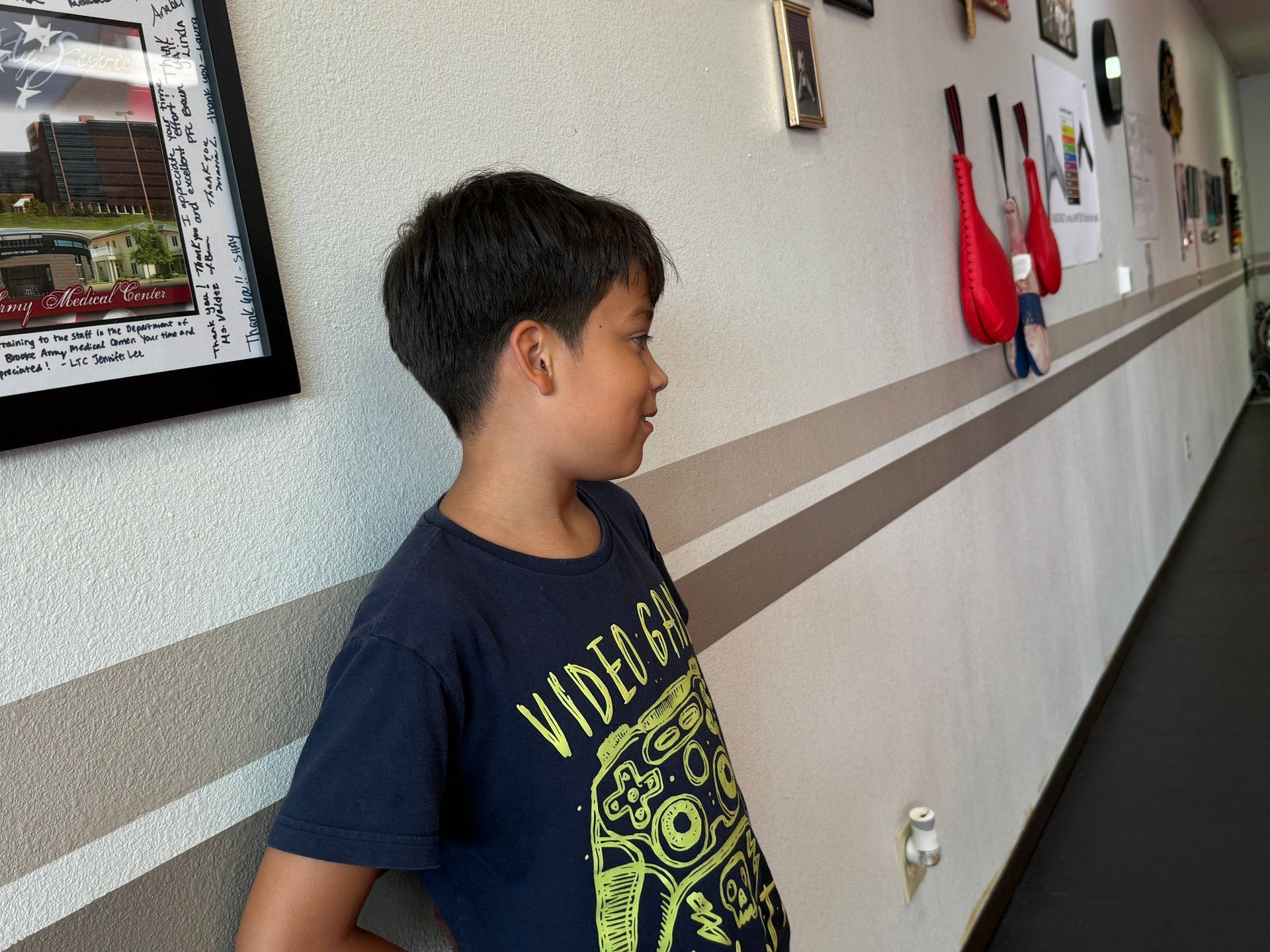 Boy standing in a hallway beside a wall with framed art and red hanging items