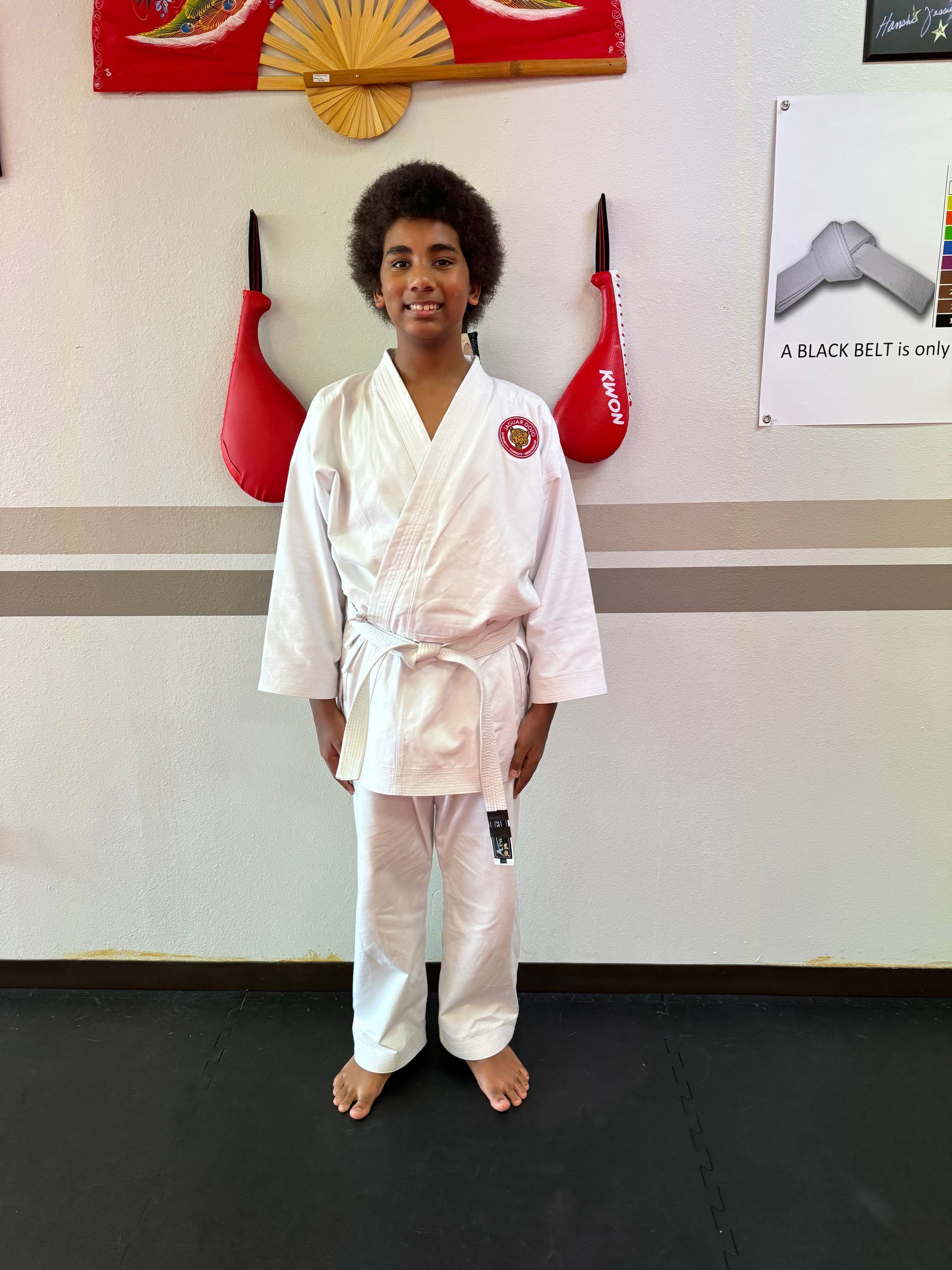 Person in a white martial arts uniform standing indoors in front of a wall display.