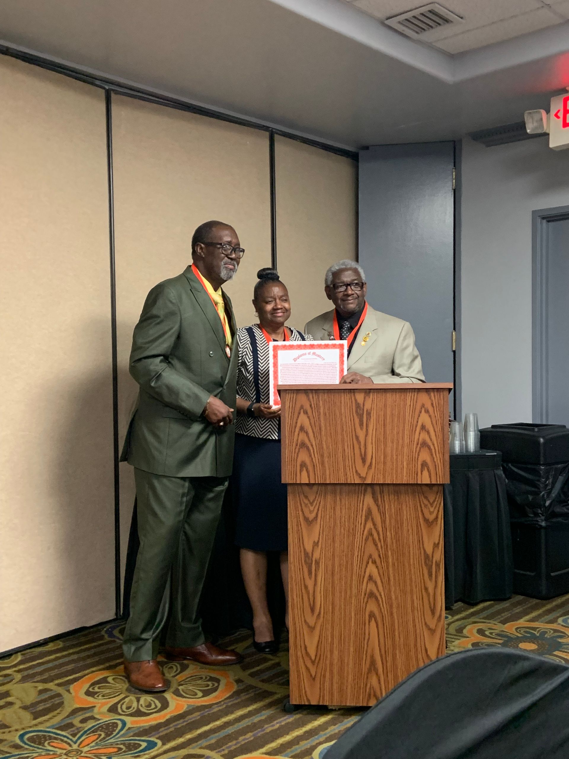 Three people posing at a podium, holding a framed certificate in a conference room.