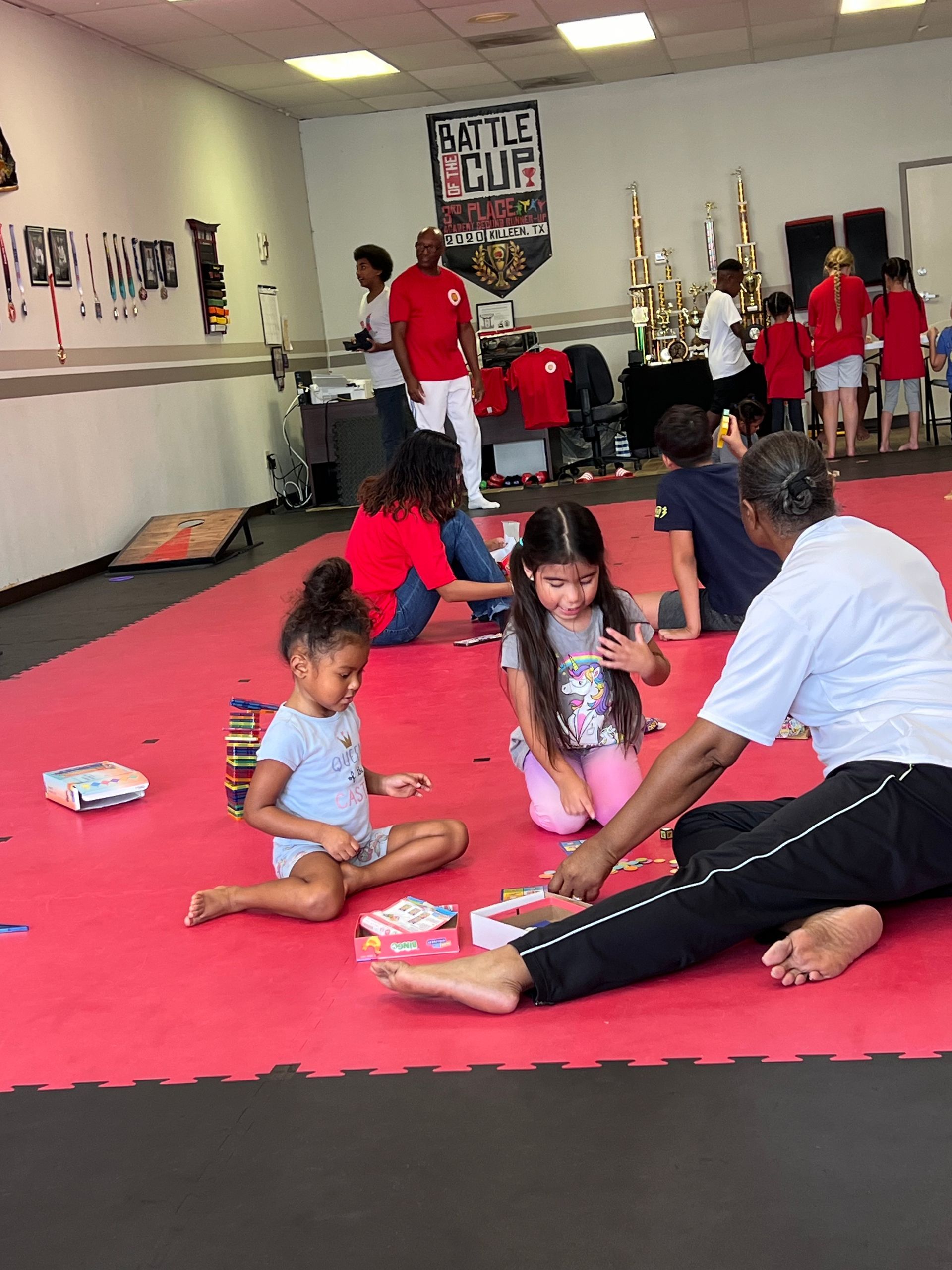 People stretching on a red mat in a gym class, with an instructor nearby and posters on the wall.