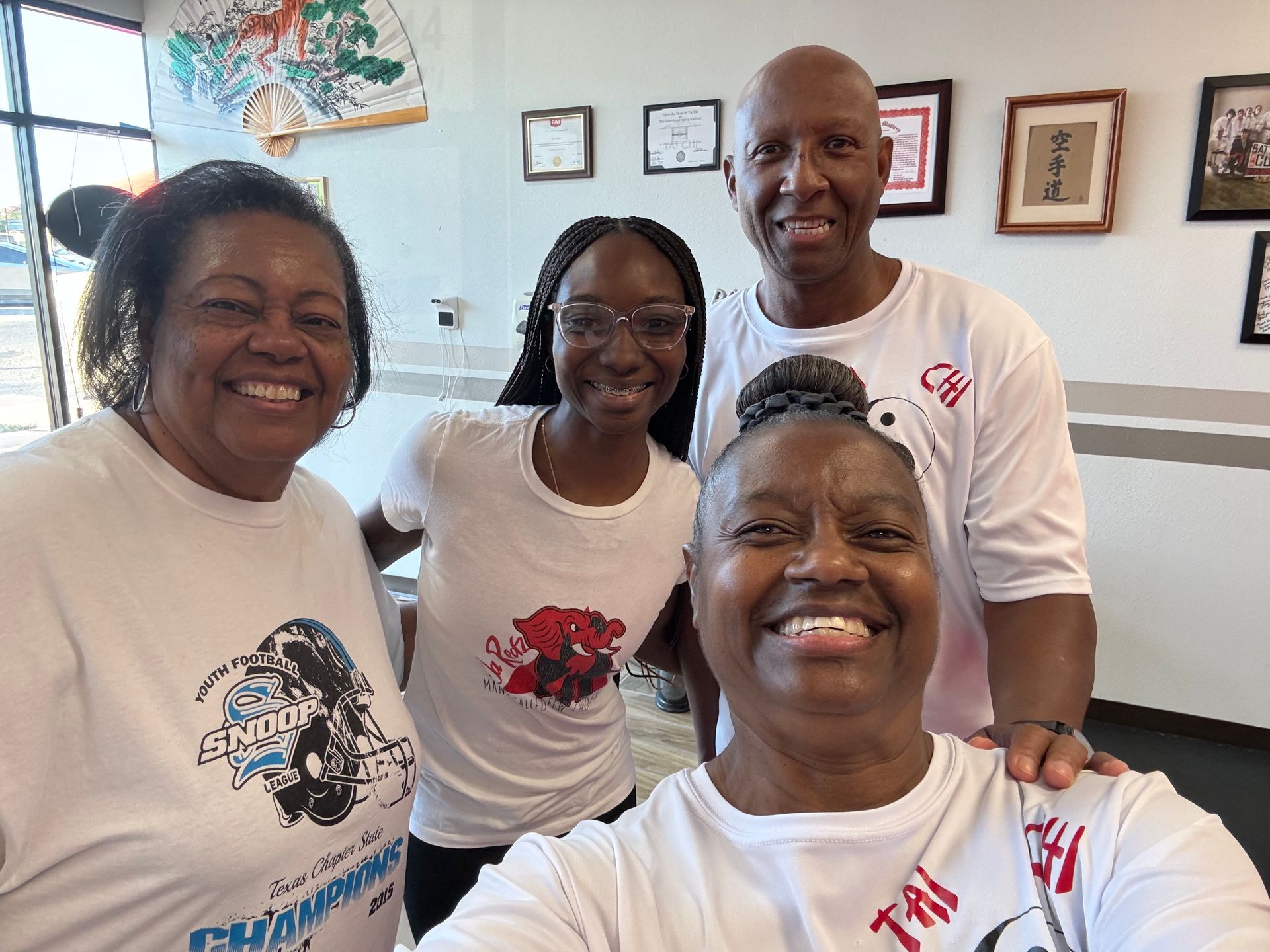 Four people smiling indoors, wearing white shirts, in front of framed wall art.