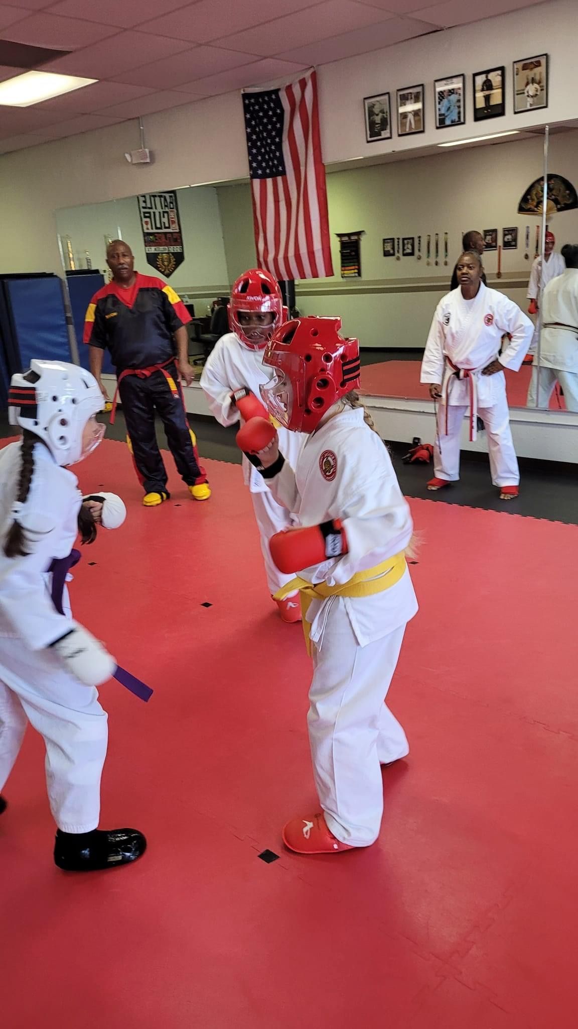 Martial arts class with children in red and white sparring gear on a red mat in a dojo