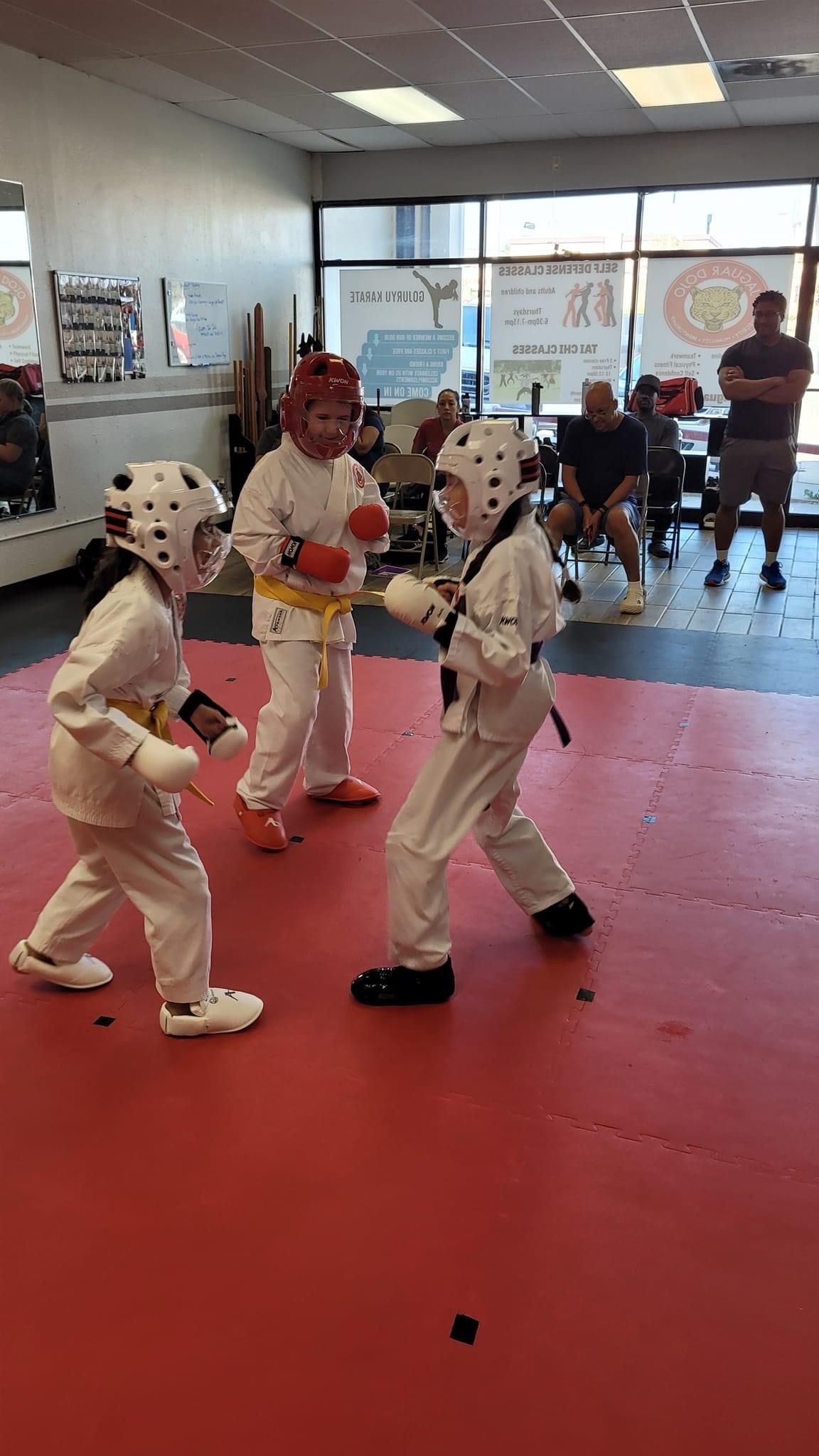 Children in white karate uniforms sparring on red mats in a martial arts studio