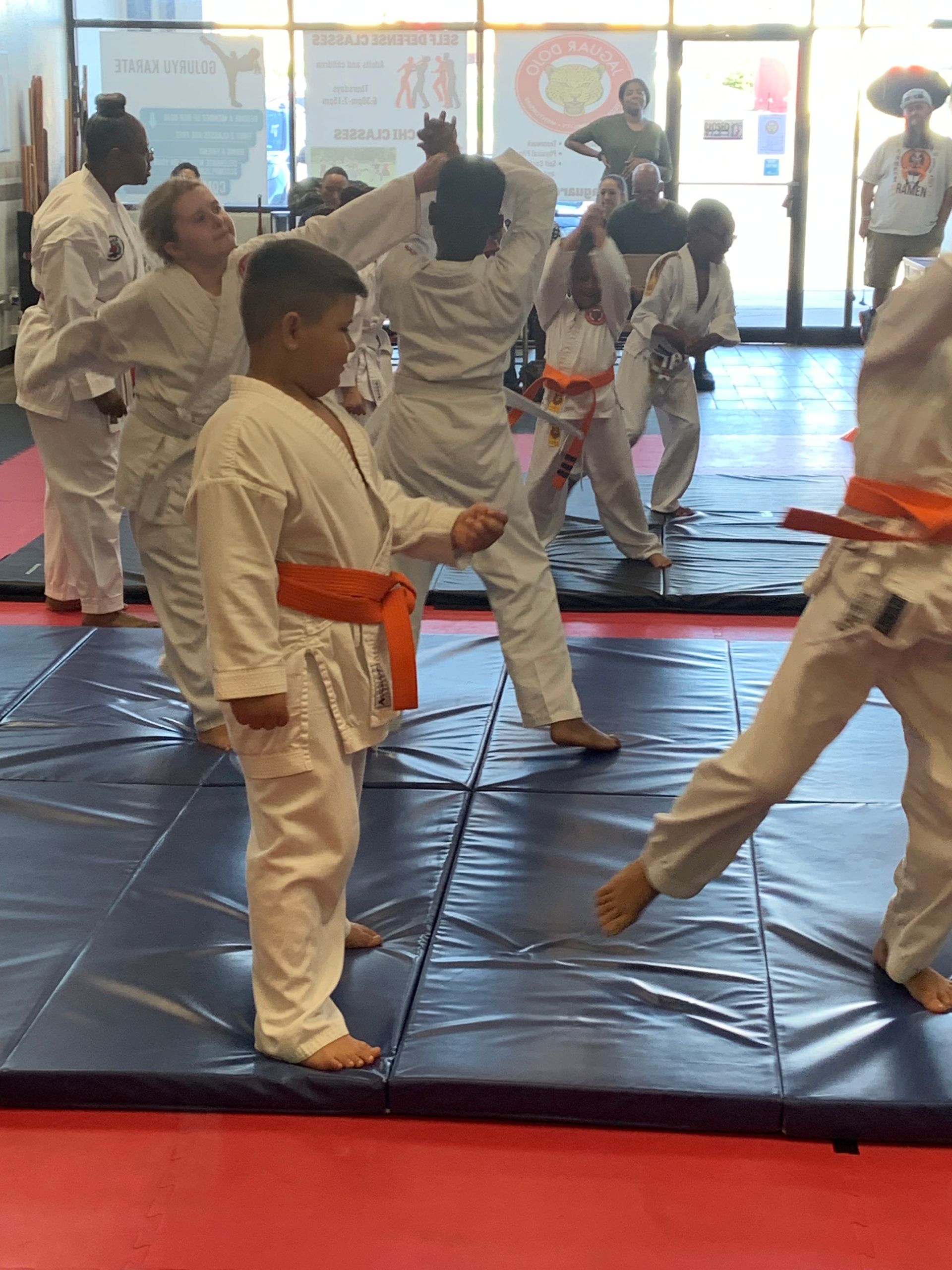 Children practicing martial arts in white uniforms on blue mats in a bright studio