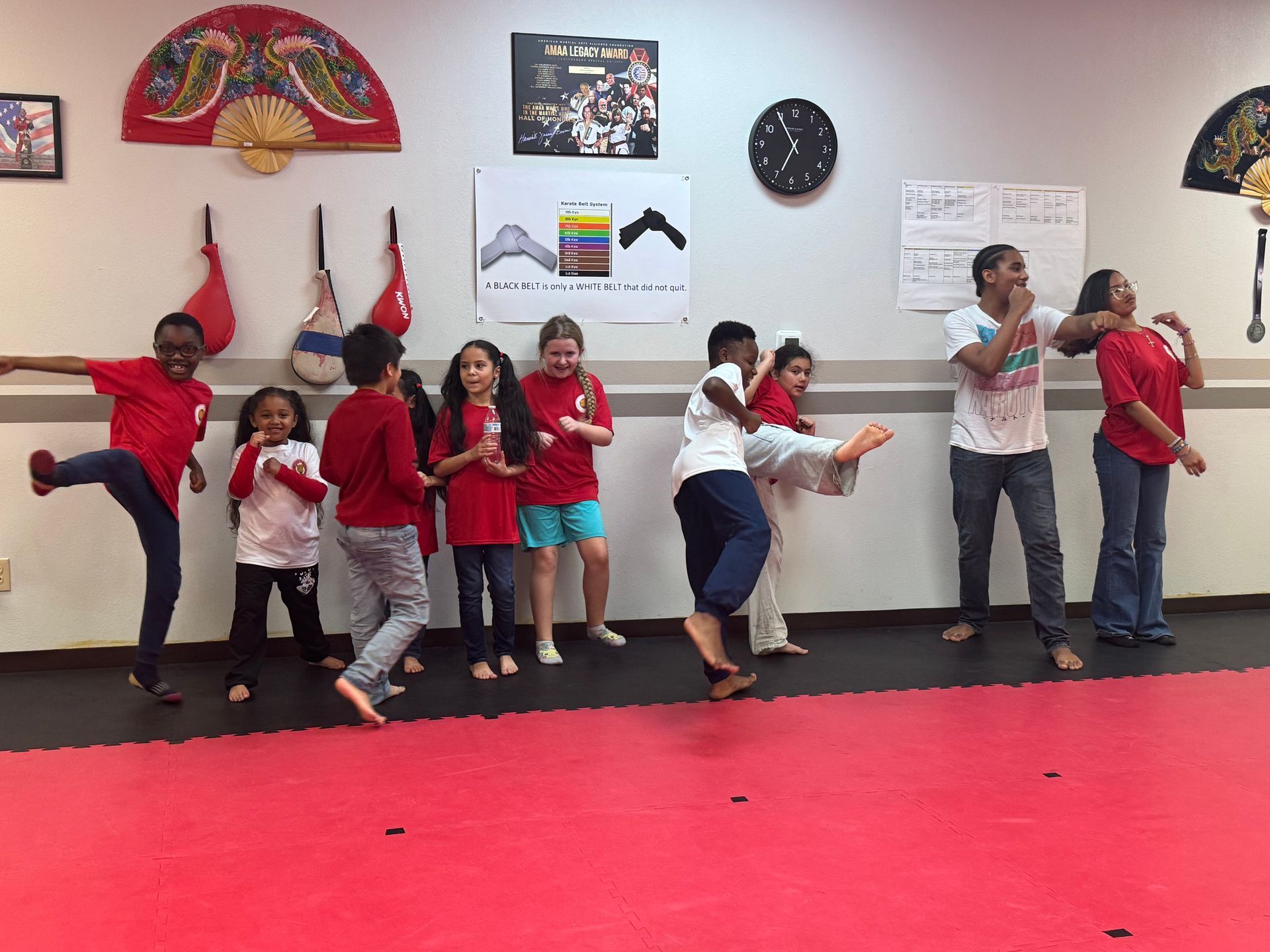 Children posing playfully in a martial arts studio, with red mats and wall decorations.