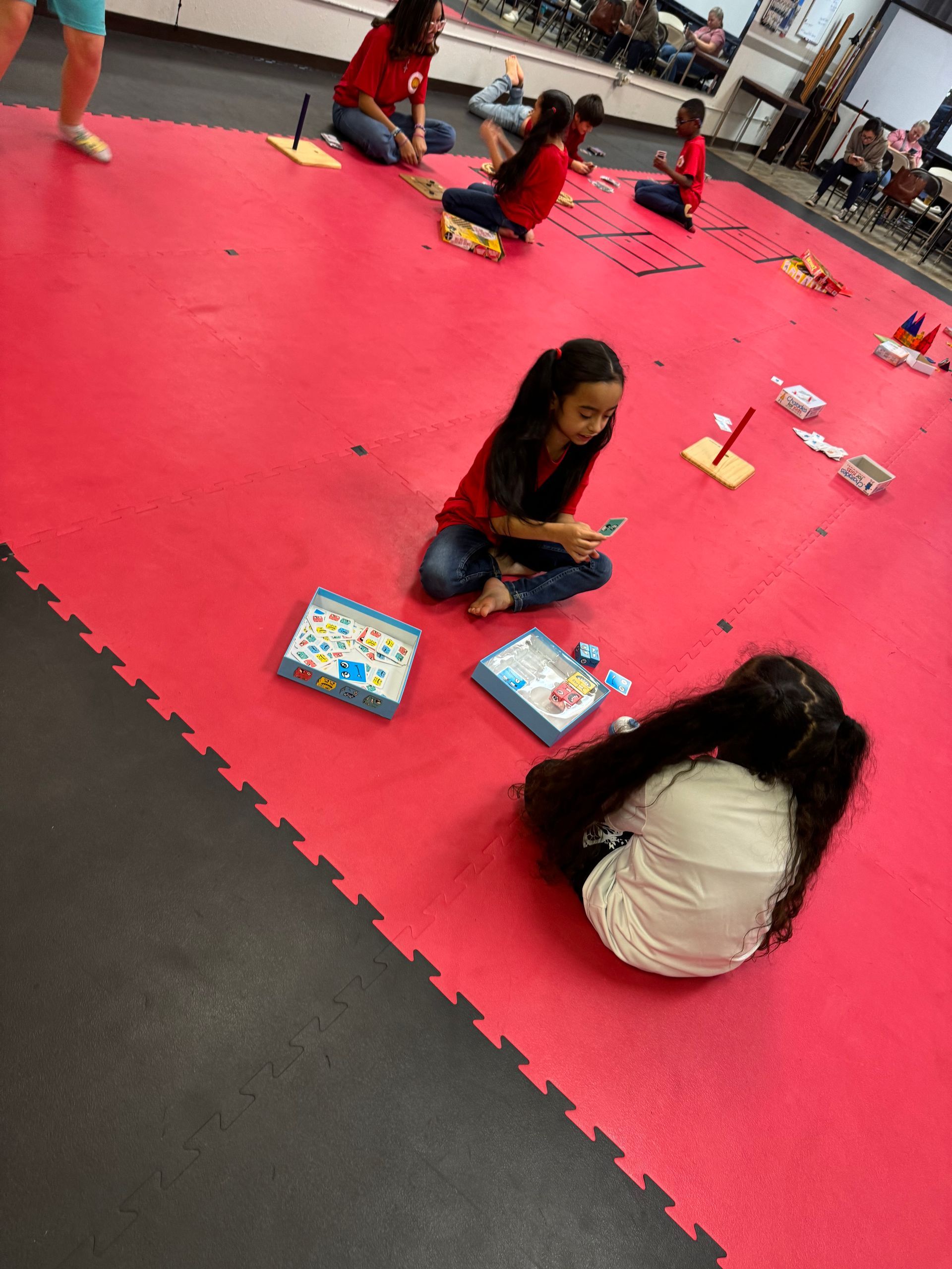 Children sitting and playing on a bright pink floor at an indoor activity area.