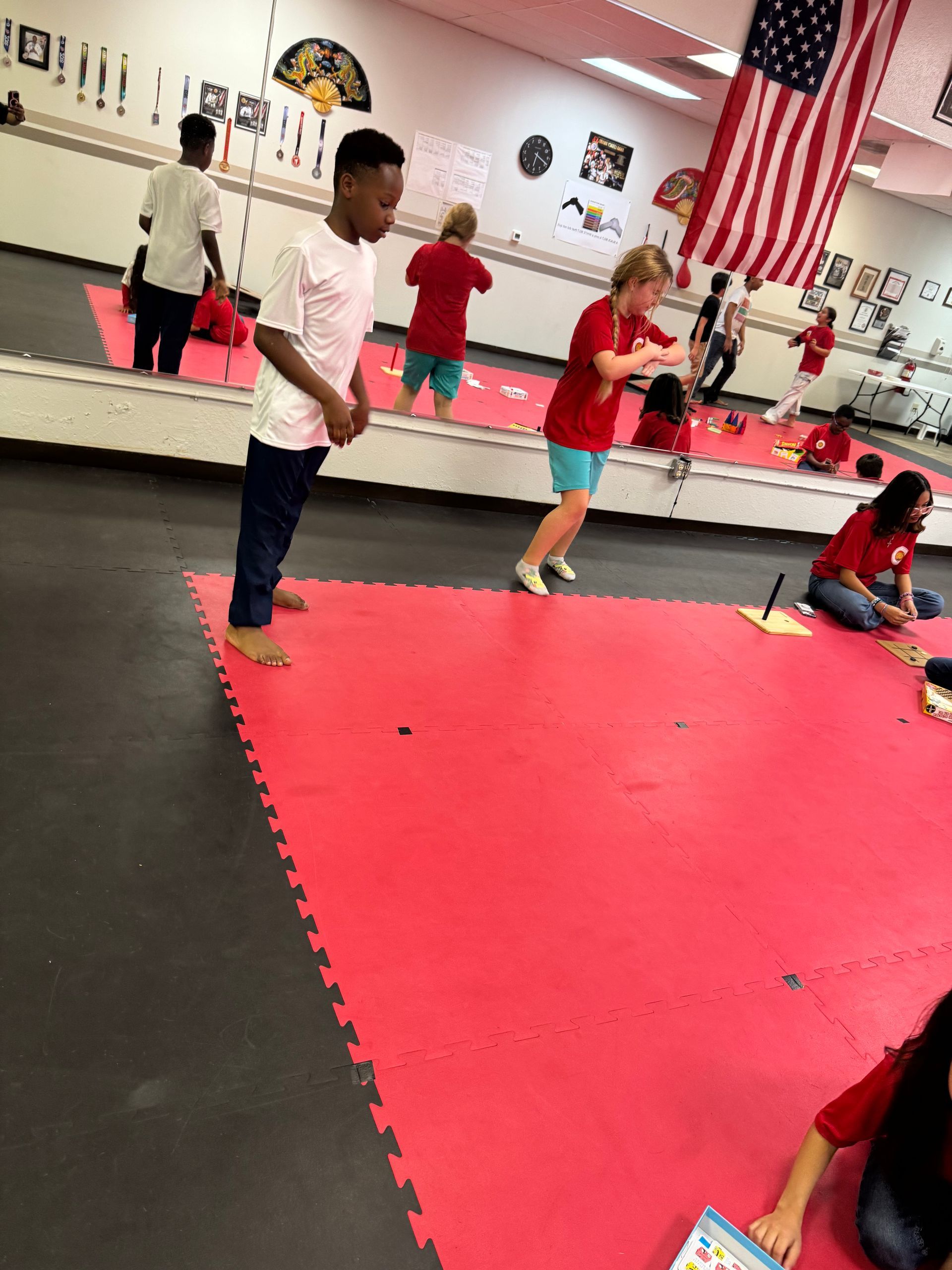 Children practicing martial arts in a dojo with red mats and a large American flag on the wall