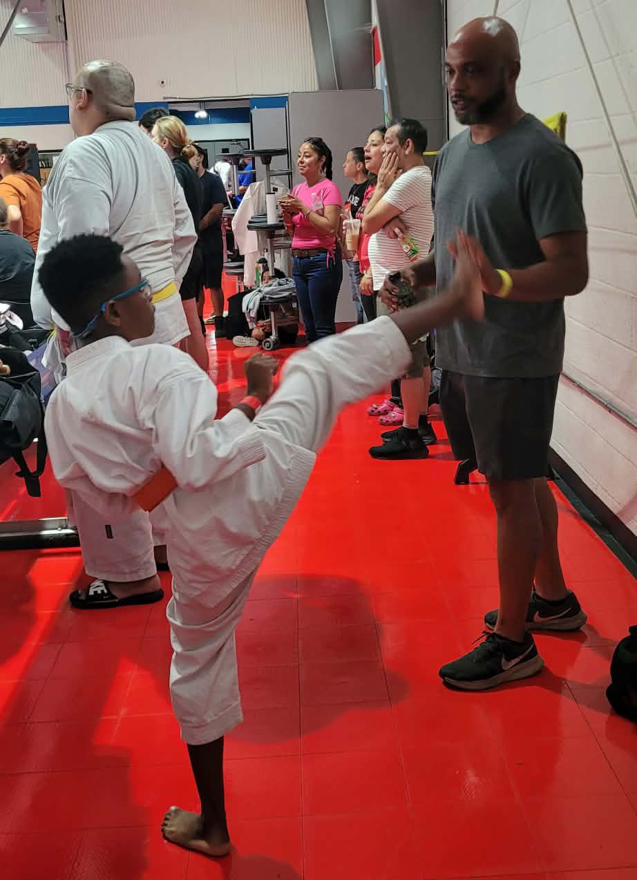 Martial arts demo on a red mat, child in white uniform kicking an instructor in gray shirt.