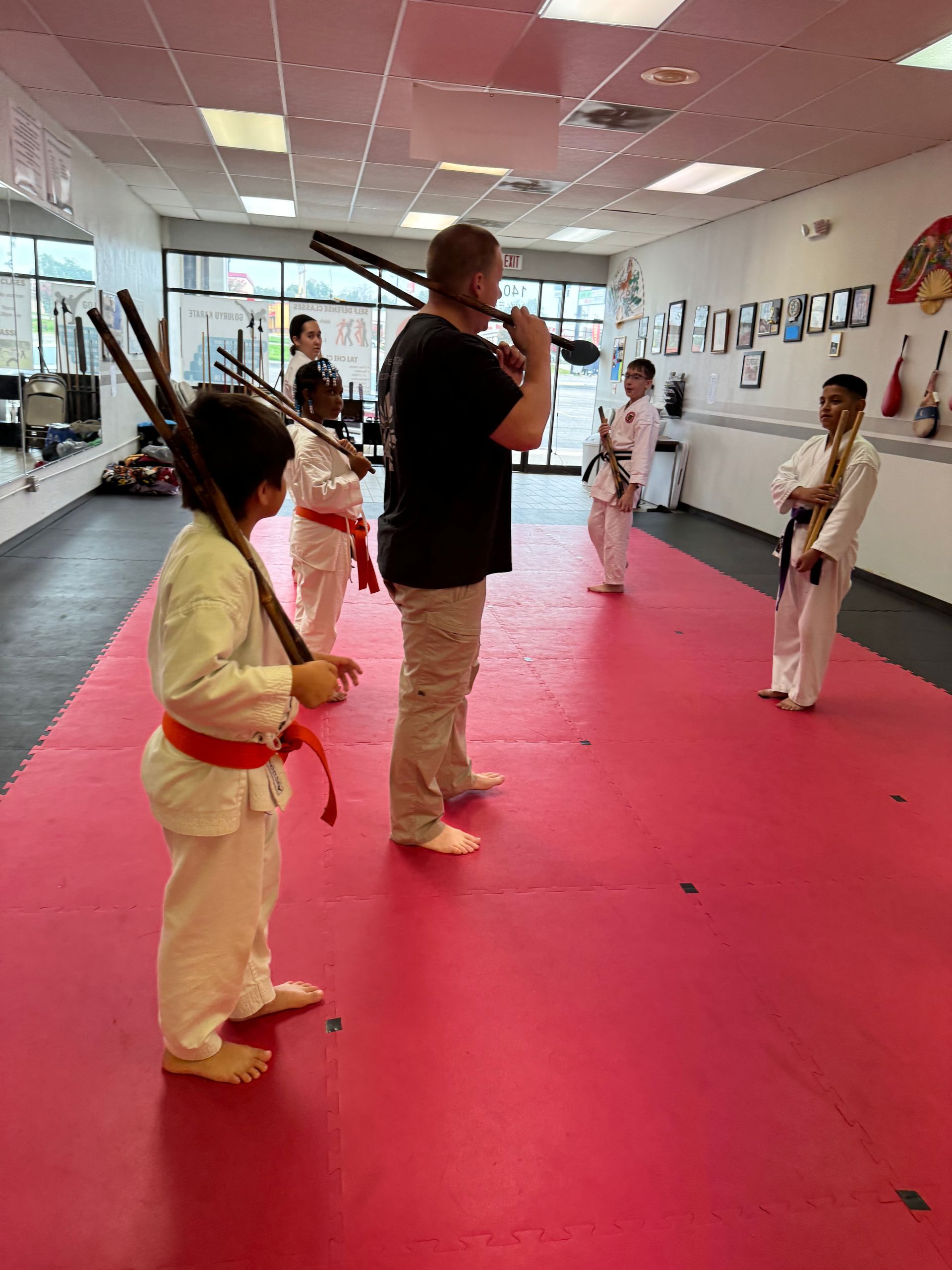 Kids practicing martial arts in a studio with a red mat and an instructor standing in front.