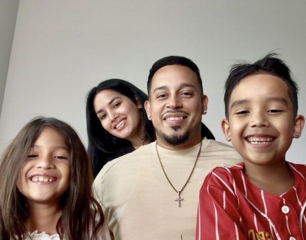 Smiling family of four posing indoors against a plain wall.