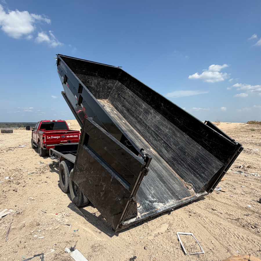 Red dump truck with raised black bed in a sandy desert area under a blue sky