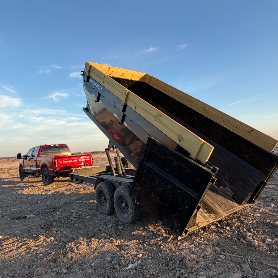 Red pickup truck tipping a dump trailer on a gravel lot at sunset