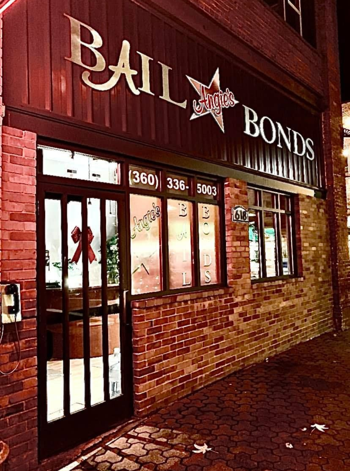 Bail bonds office with red brick facade and sign. Dark exterior, lit windows, and a Christmas decoration.