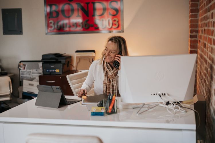Woman talking on phone at a desk in an office, working on computer, with a tablet.