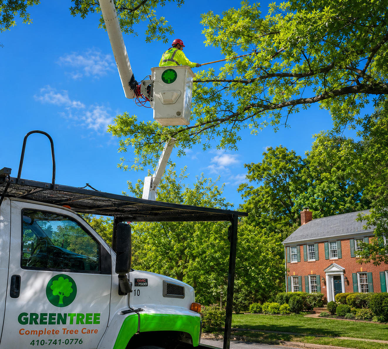 Tree service worker in a bucket lifts near a brick house under a bright blue sky