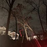 Dark yard with bare trees and a house lit by porch lights at night