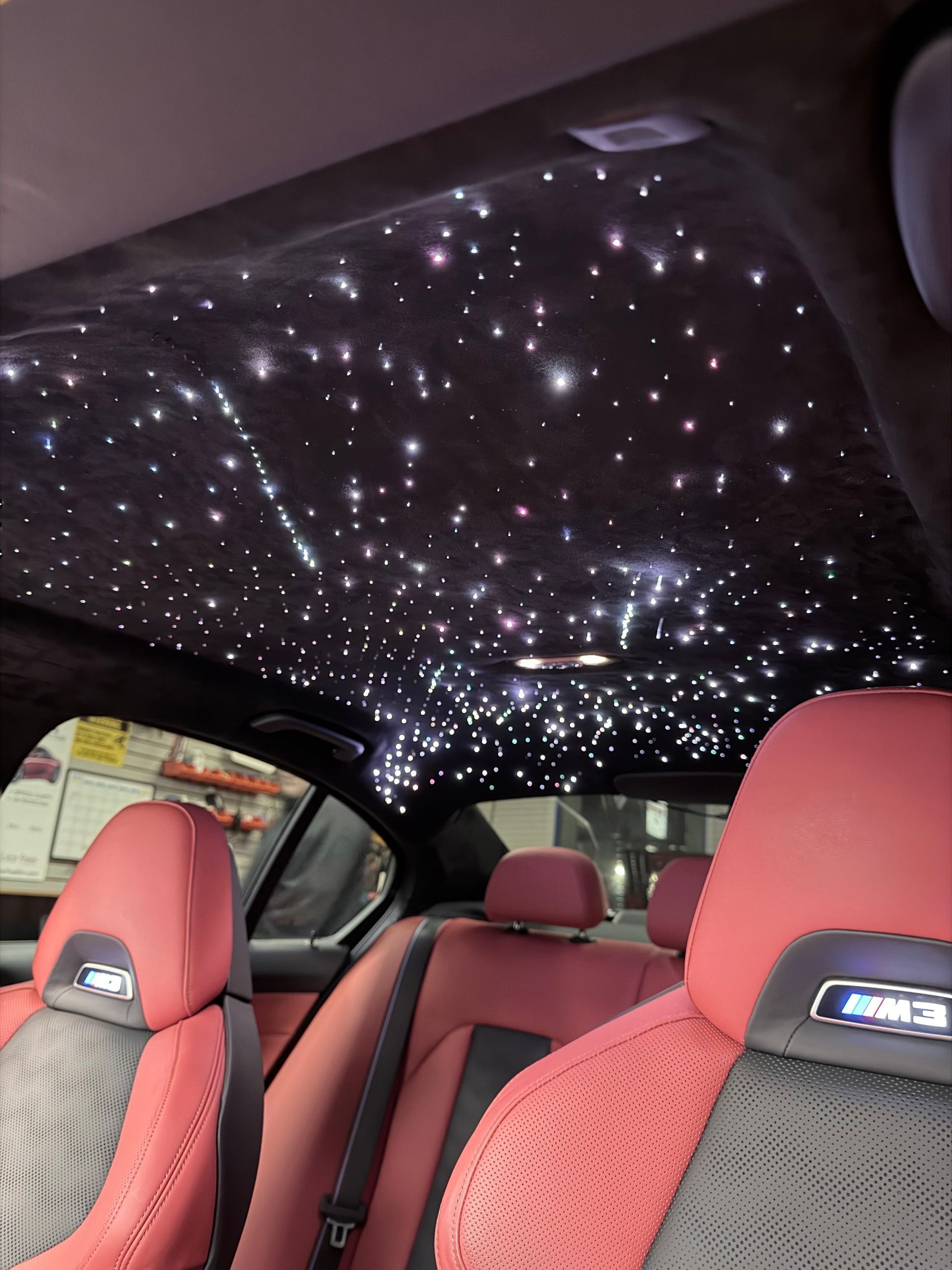 The interior of a car with a starlight headliner, featuring red leather seats with BMW M badges on the headrests.